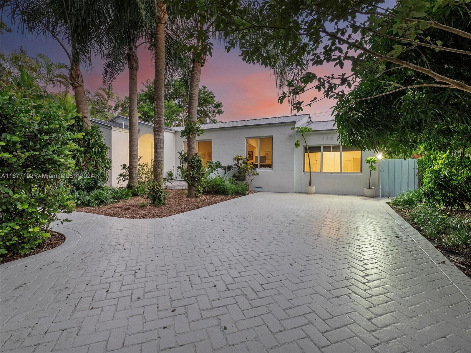 Modern white house with a broad paved driveway and tropical landscaping at dusk.