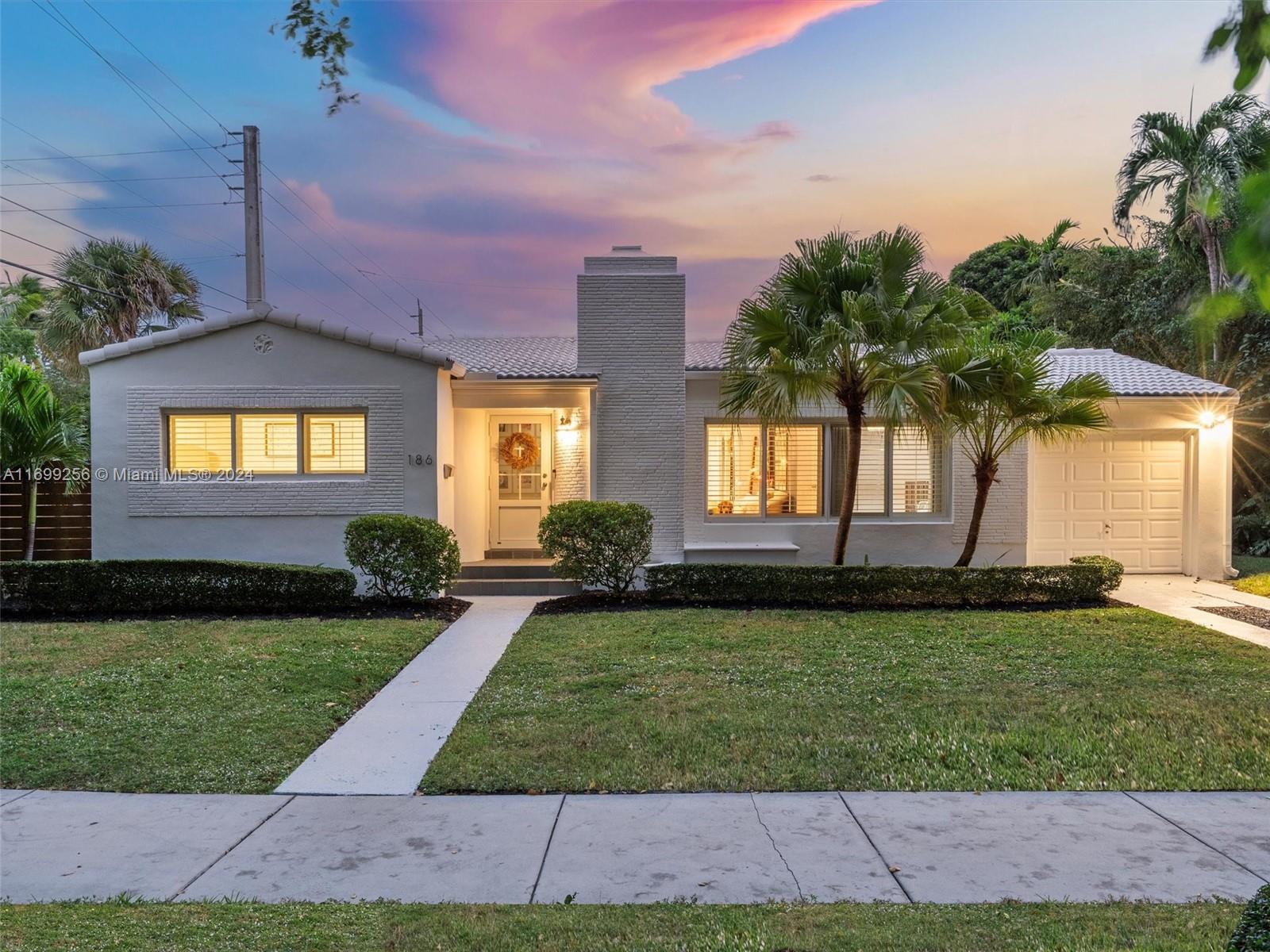 Gray brick single-story home with a central chimney, palm trees, and a pink dusk sky.