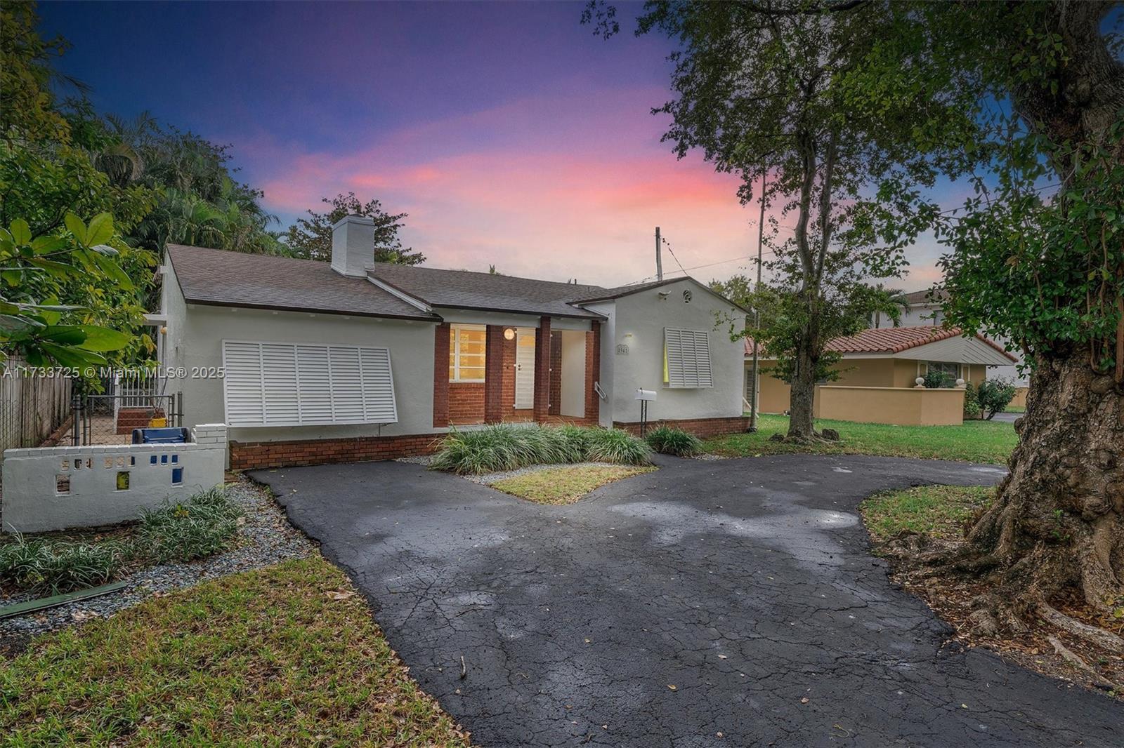 Single-story stucco house with brick accents and a broad driveway beneath a pink dusk sky.