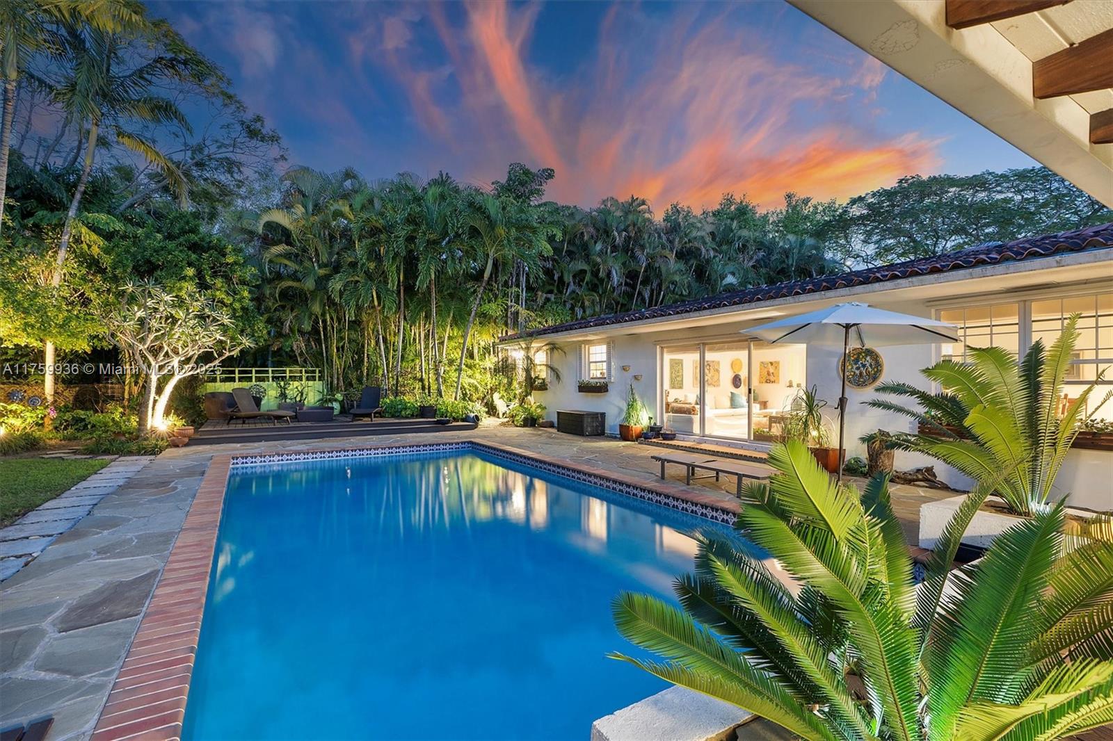 Backyard pool beside a single-story home, surrounded by tropical palms at dusk.