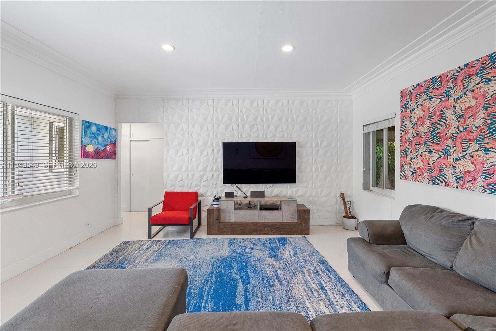 Living room with a sculpted white TV wall, red accent chair, gray sofa, and blue rug.