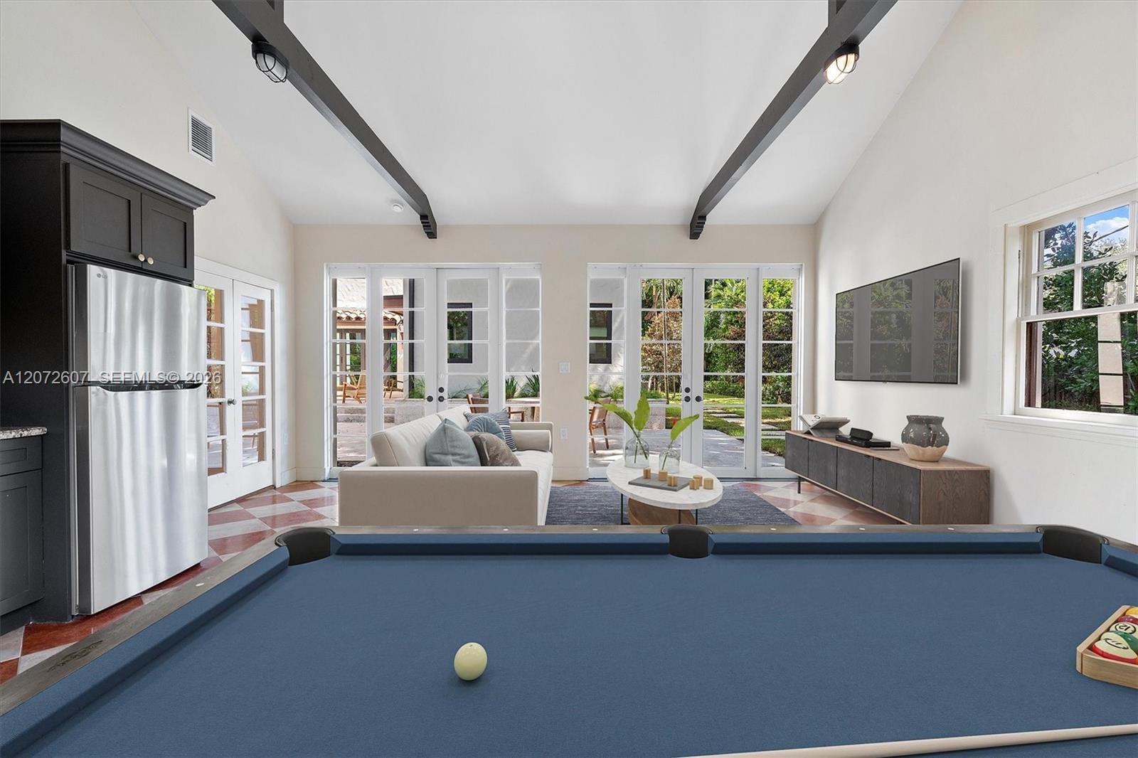 Furnished game room with a blue pool table, exposed ceiling beams, and French doors to a garden patio.