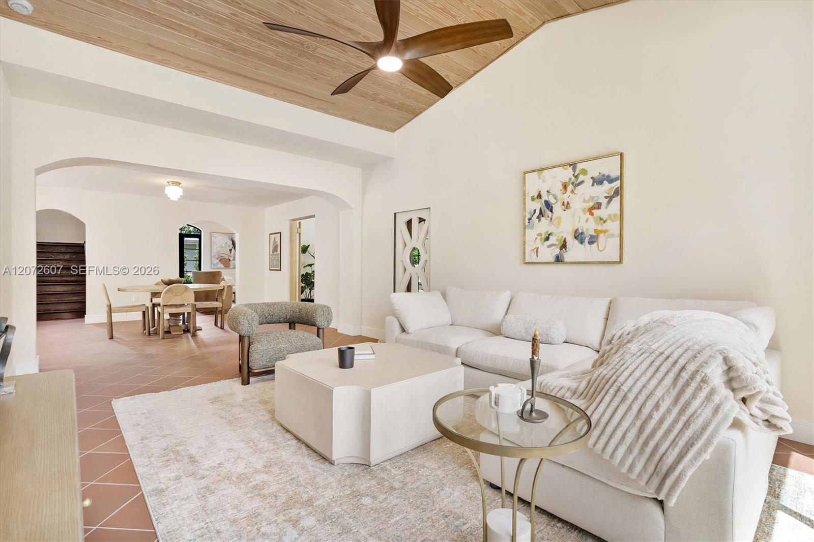 Living room with a white sectional, terracotta tile floors, and a wood-plank ceiling with a ceiling fan.