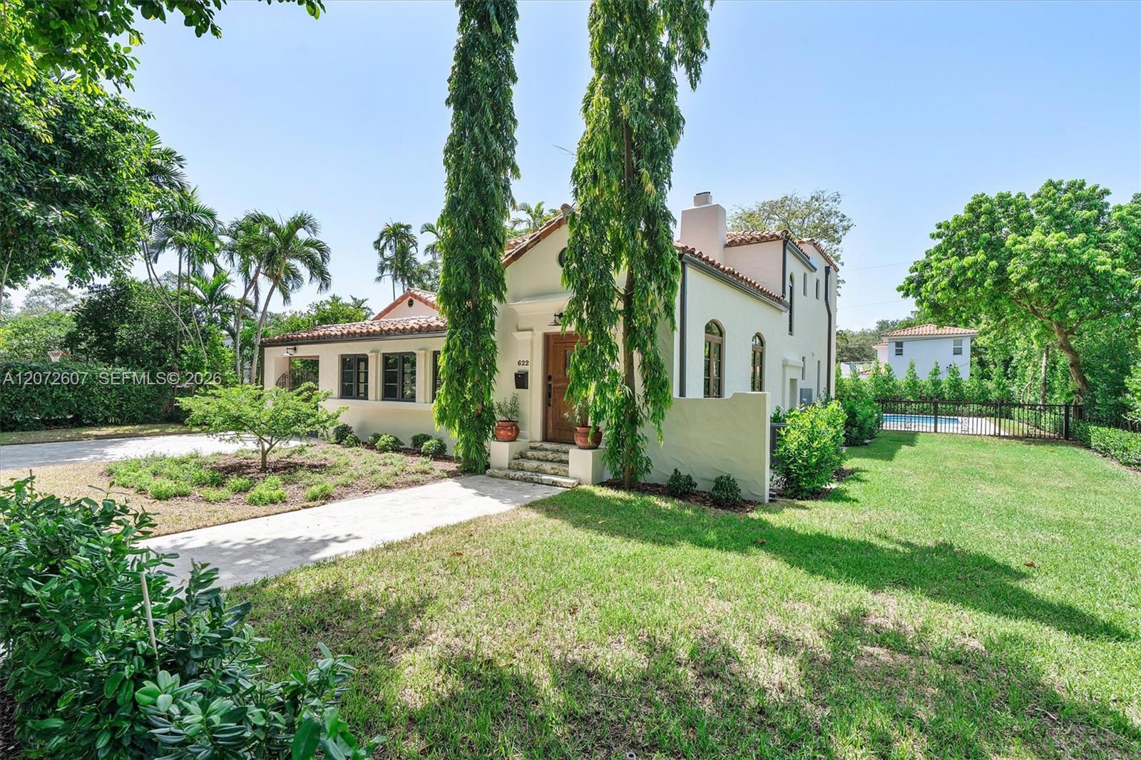 White stucco home with a red tile roof, arched windows, and a fenced pool beside the lawn.