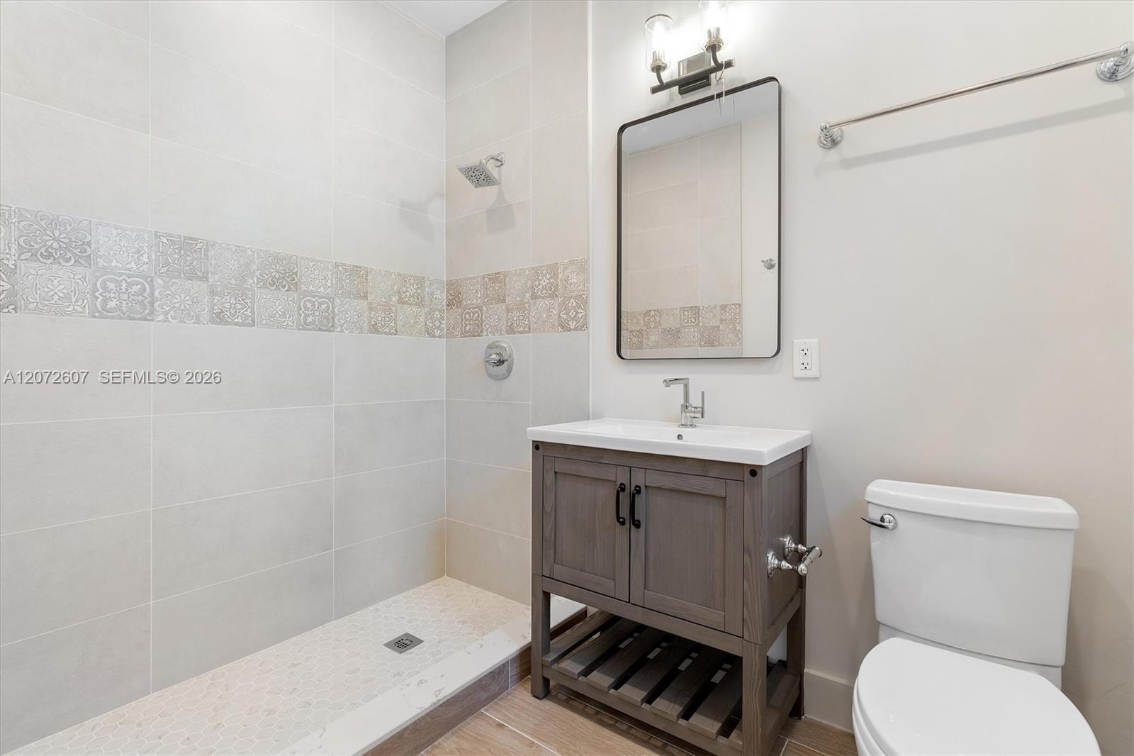 Bathroom with a patterned-tile walk-in shower, gray wood vanity, and white toilet.