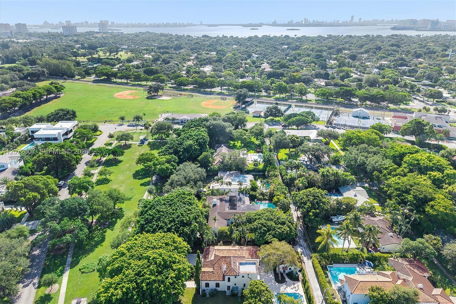 Aerial view of a leafy neighborhood, park and sports fields, with the bay and city skyline in the distance.