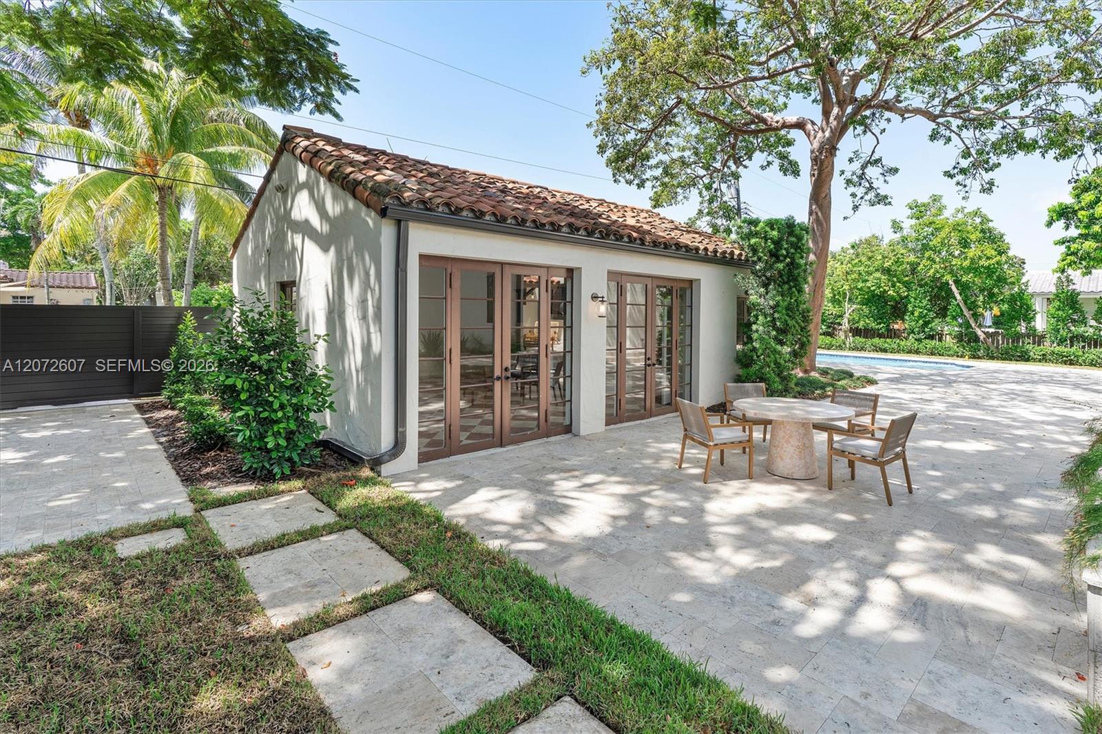 Backyard patio with a tiled-roof outbuilding, French doors, outdoor dining set, and swimming pool.