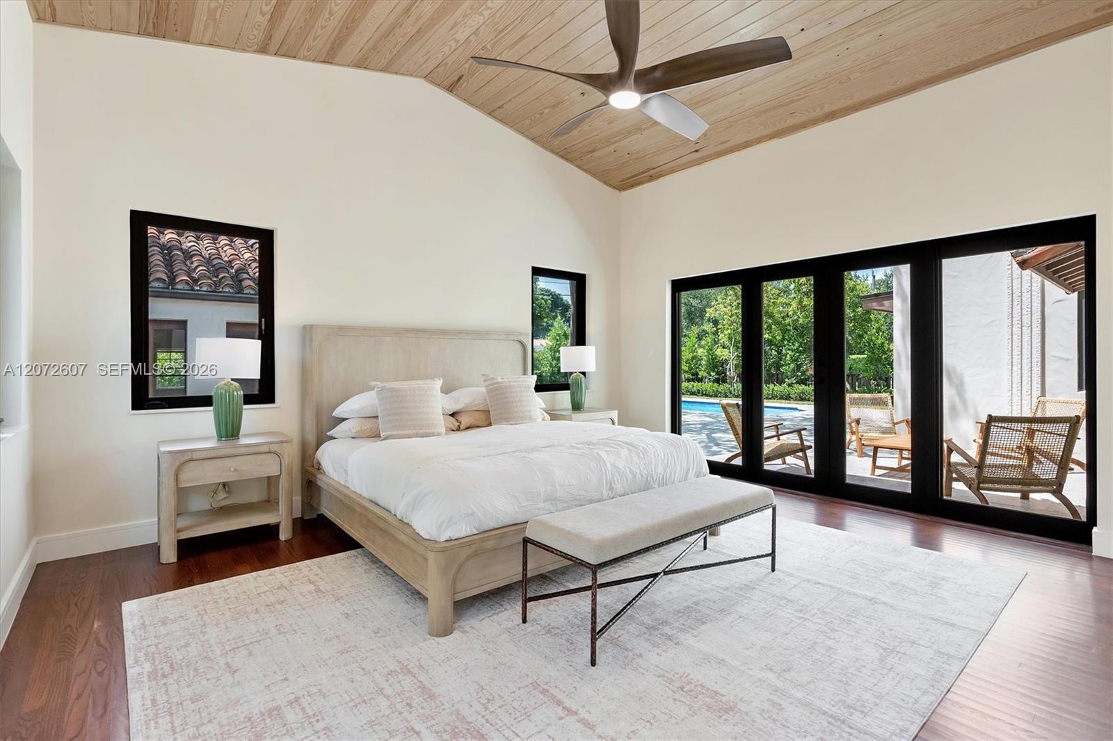 Bedroom with a vaulted wood ceiling and black-framed doors opening to a poolside patio.
