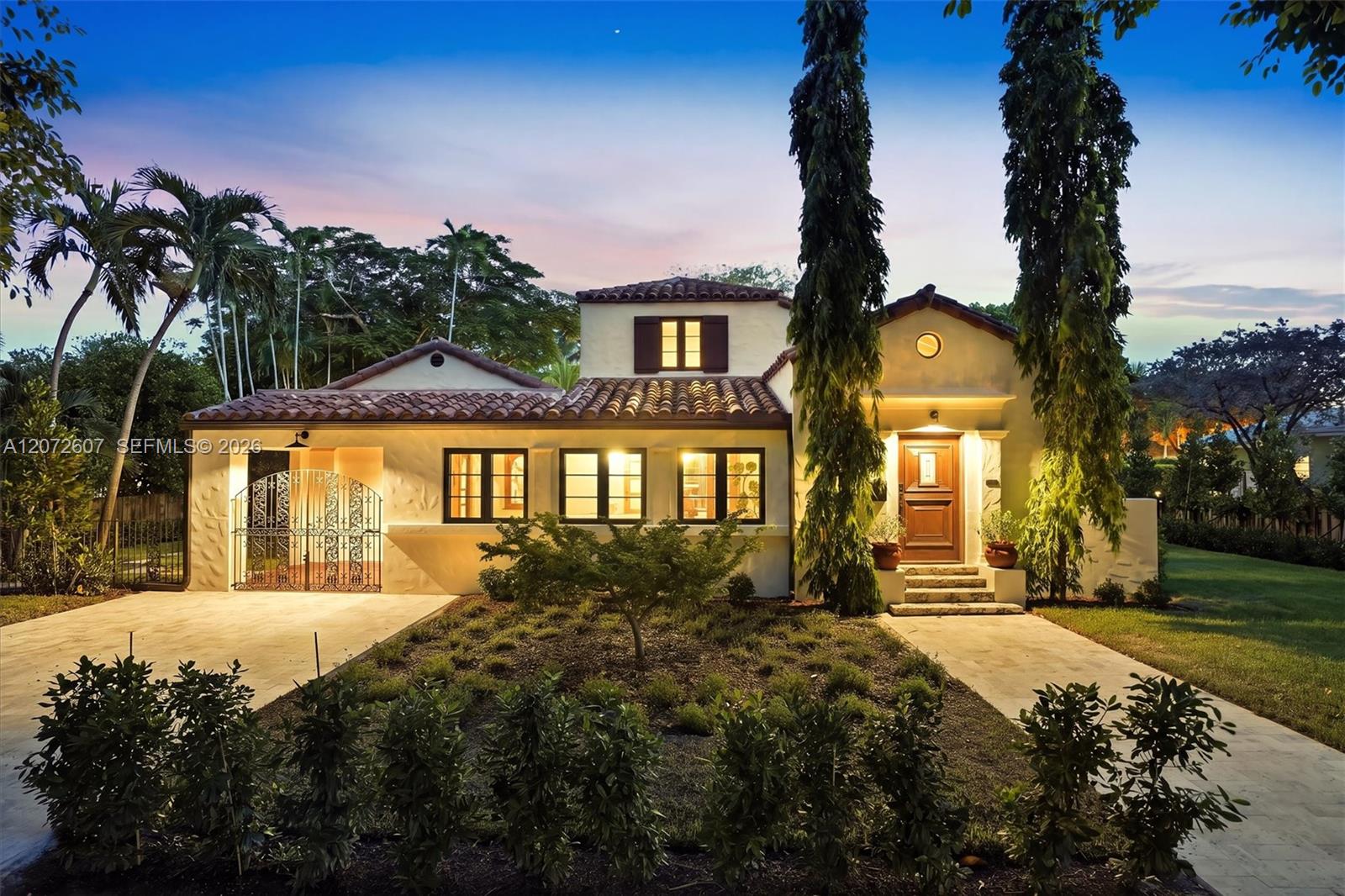 Two-story stucco home with a tile roof, ornate entry gate, and warmly lit windows at dusk.