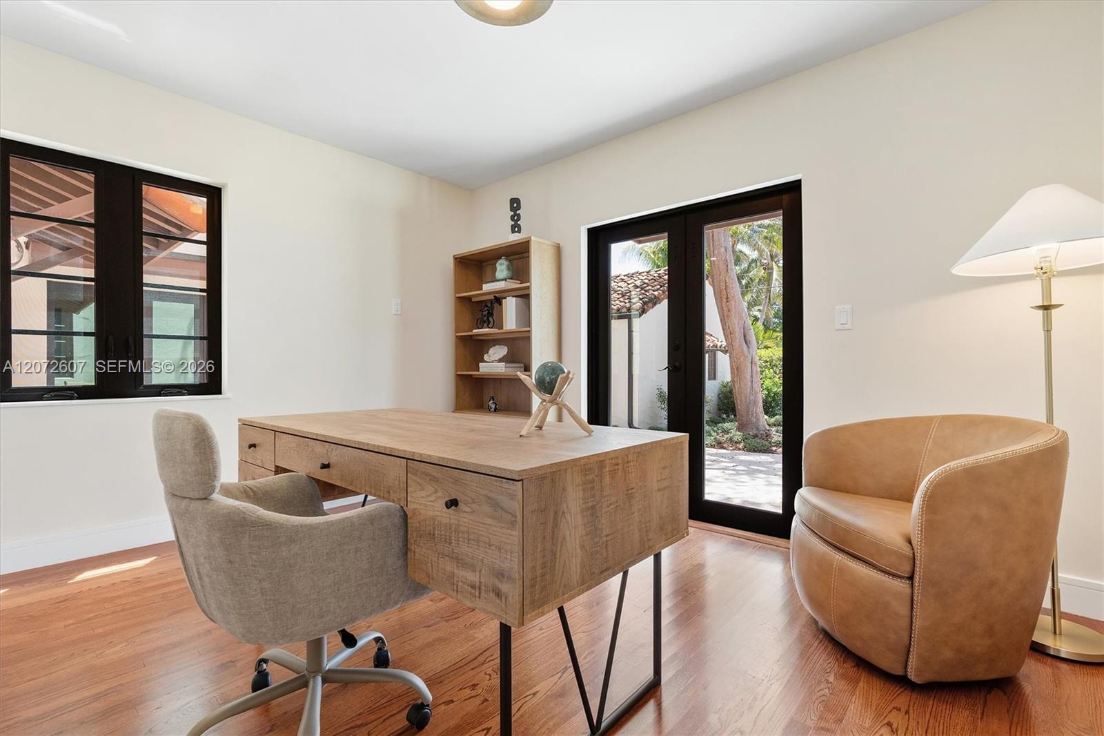 Furnished home office with a wooden desk and chairs beside glass doors opening to a courtyard.