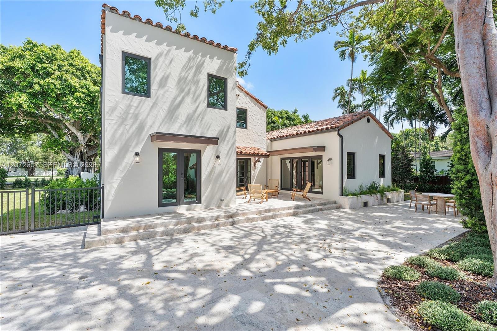 White stucco home with terracotta tile roofs and a furnished courtyard beneath tropical trees.