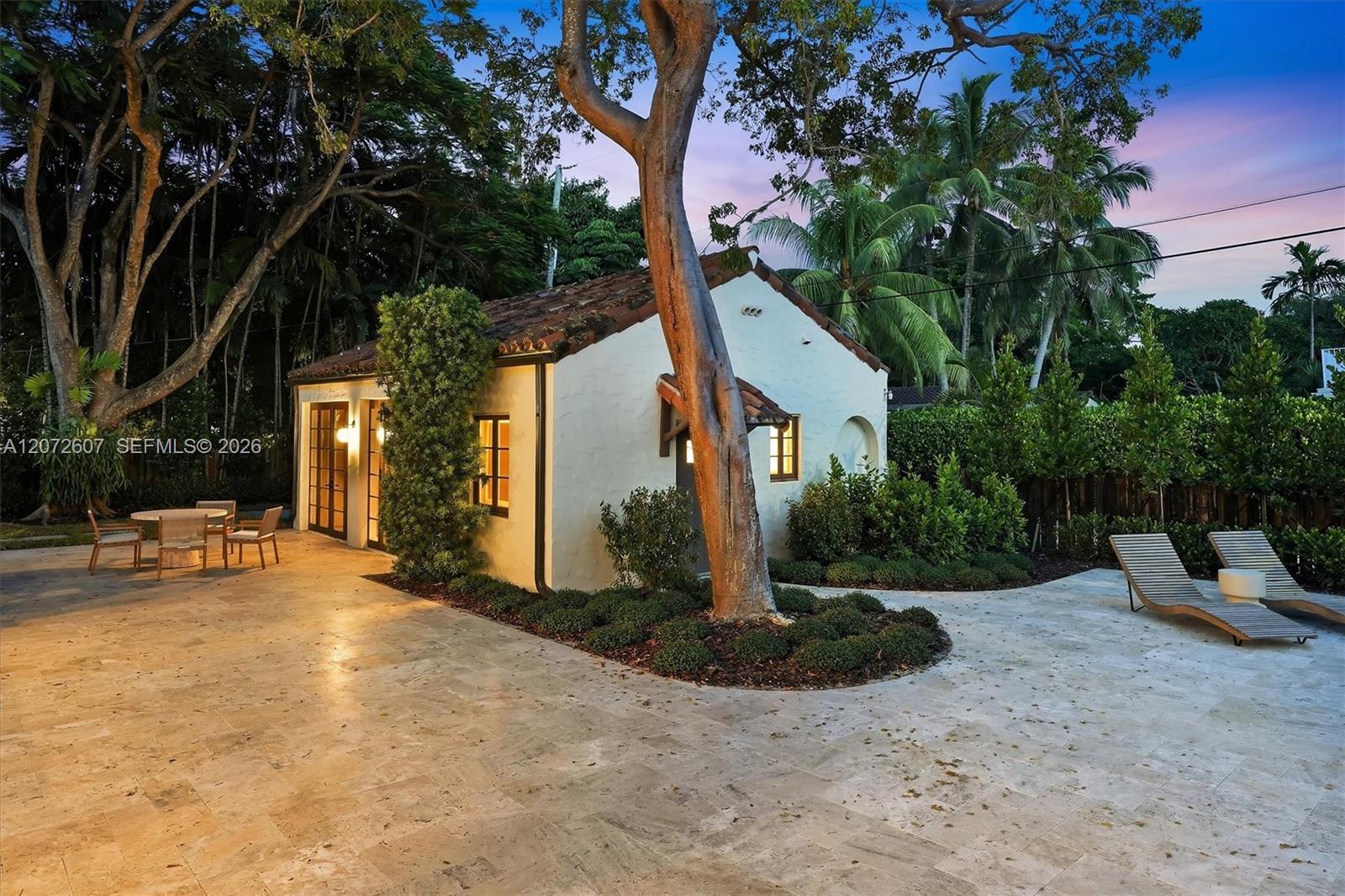 White stucco home with a terracotta roof, tropical landscaping, and a stone patio at dusk.