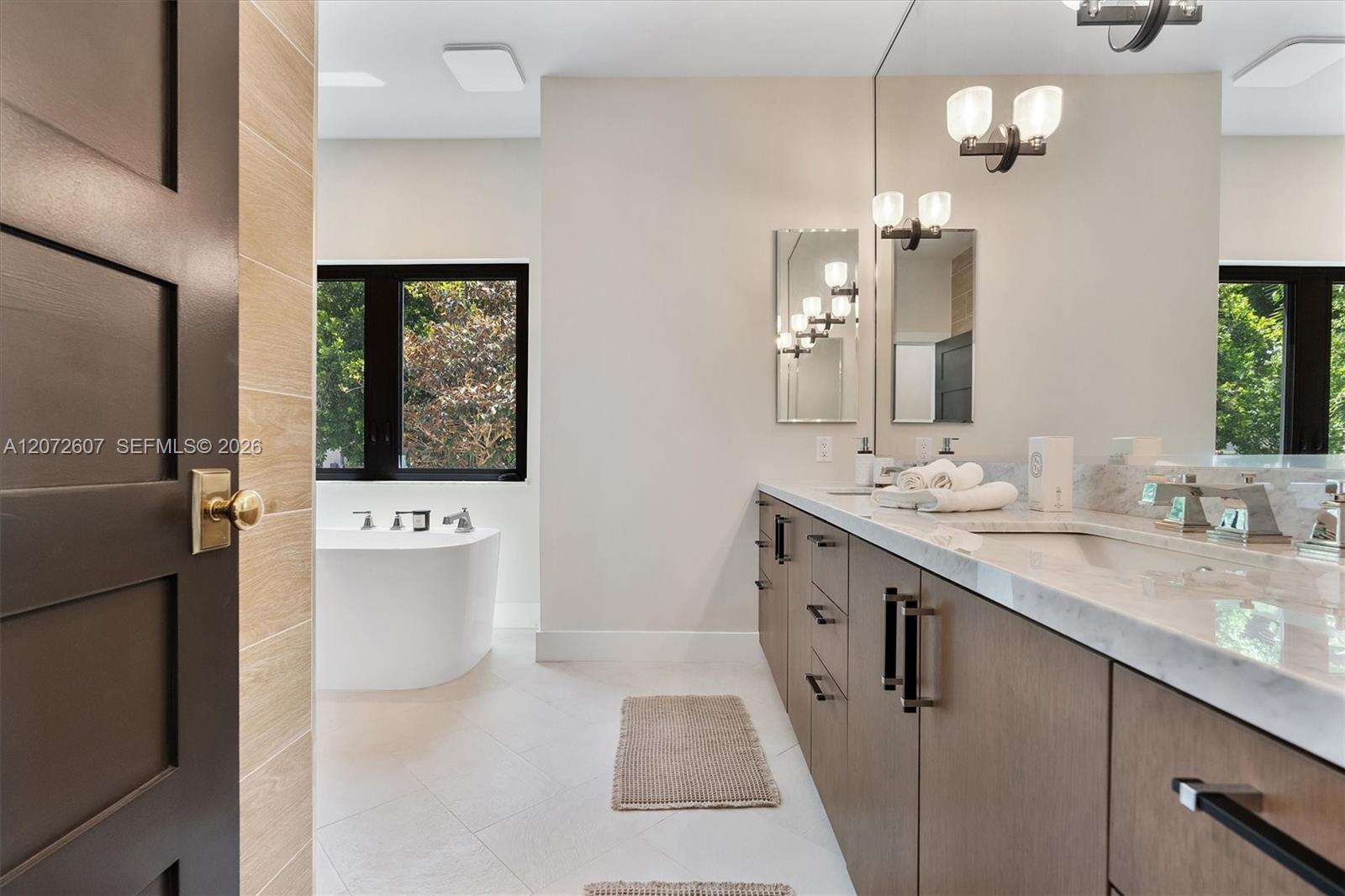 Bathroom with a long double vanity and freestanding soaking tub beside black-framed windows.