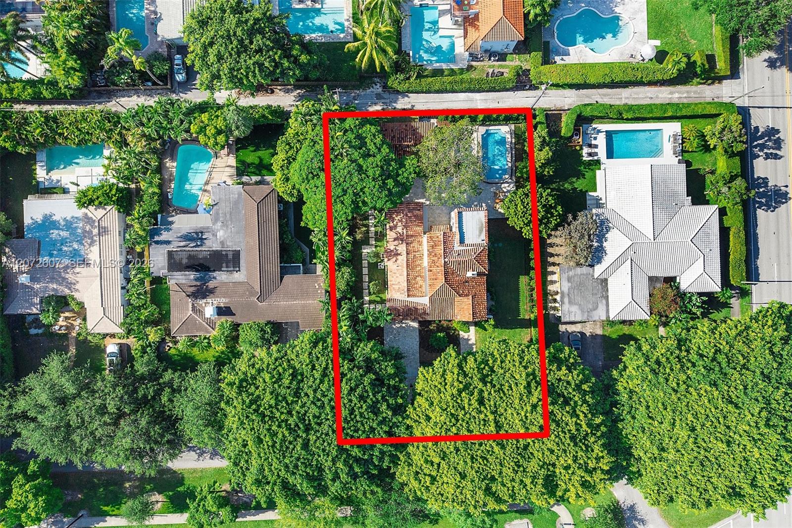 Aerial view of a tree-filled property with a red-outlined lot, tiled-roof house, and swimming pool.