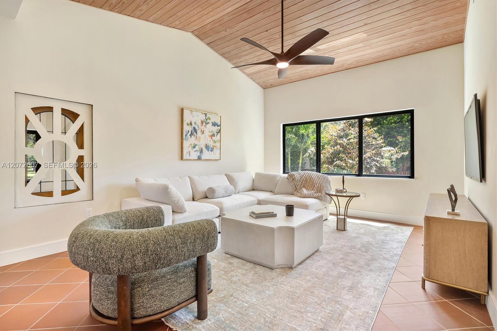 Living room with a white sectional, terracotta tile floor, and vaulted wood ceiling.