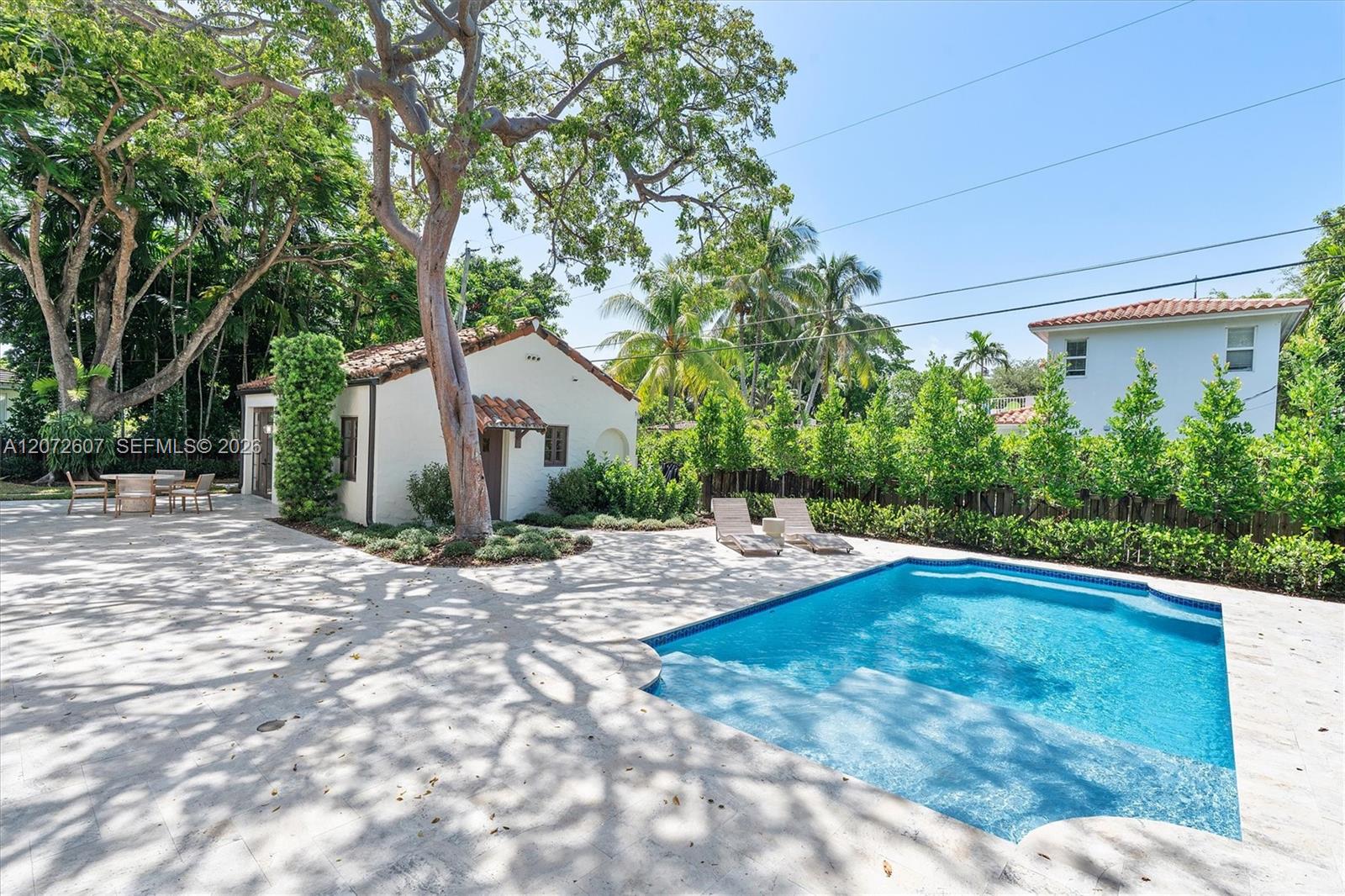 Backyard pool beside a tile-roofed house, with a shaded stone patio and tropical landscaping.