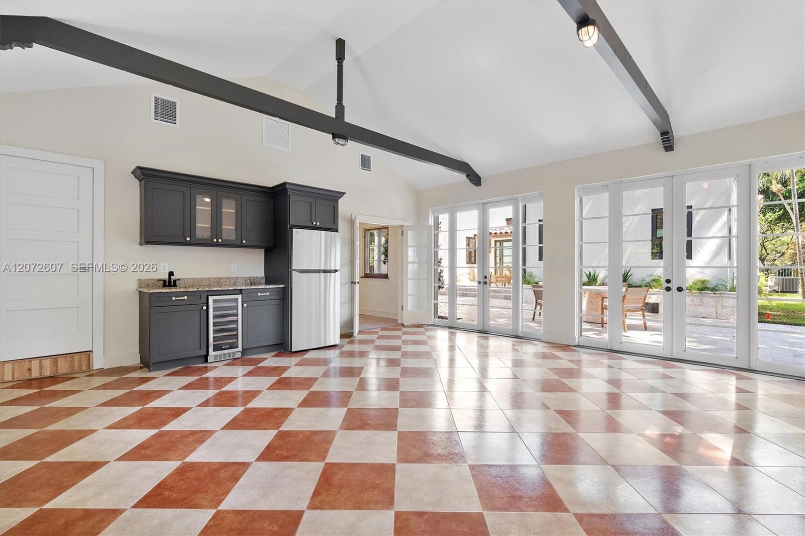 Open kitchen and living area with checkerboard tile, dark cabinetry, and French doors to a patio.