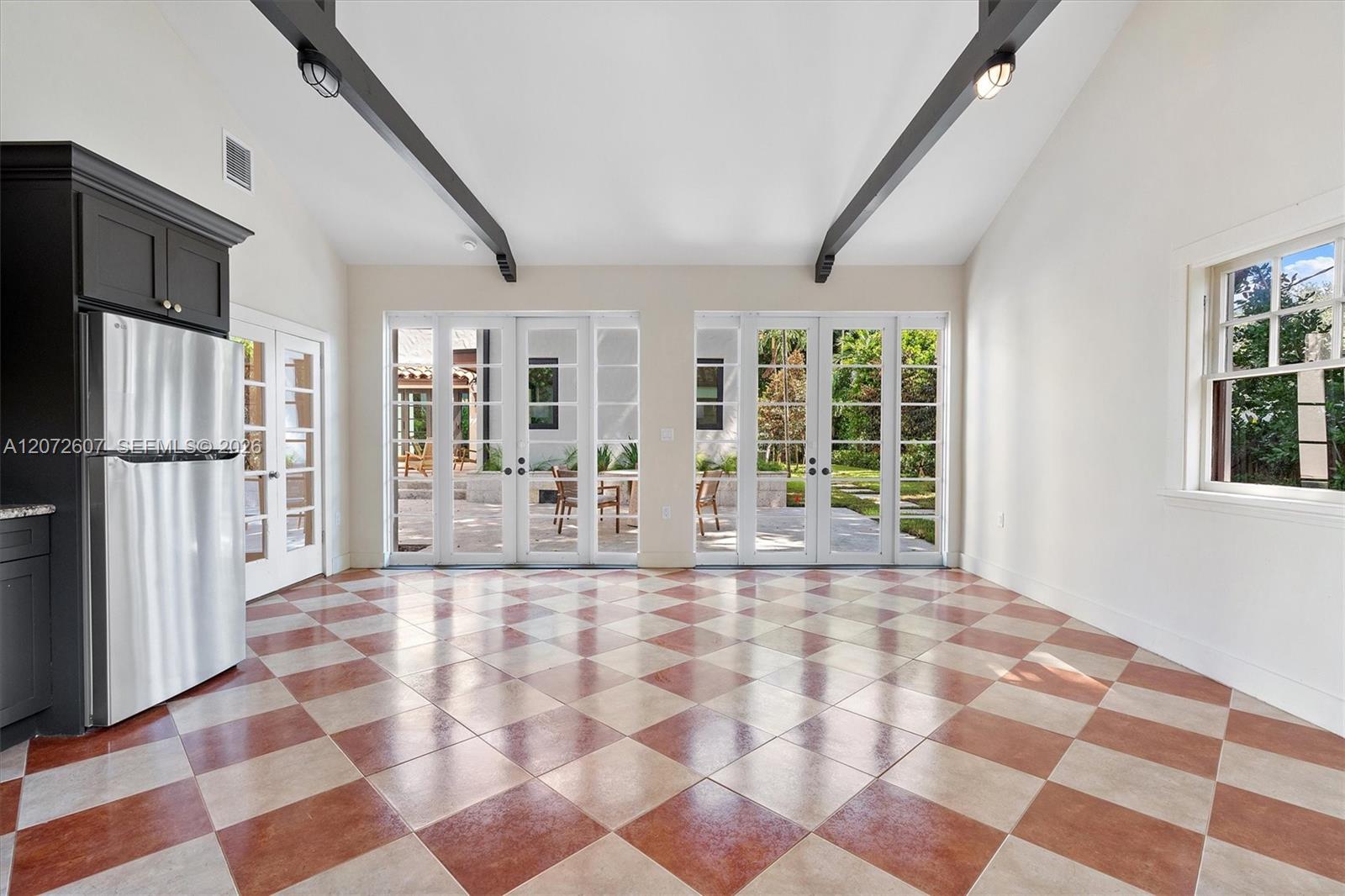 Vacant kitchen with checkerboard tile floors, dark cabinetry, and French doors opening to a garden patio.