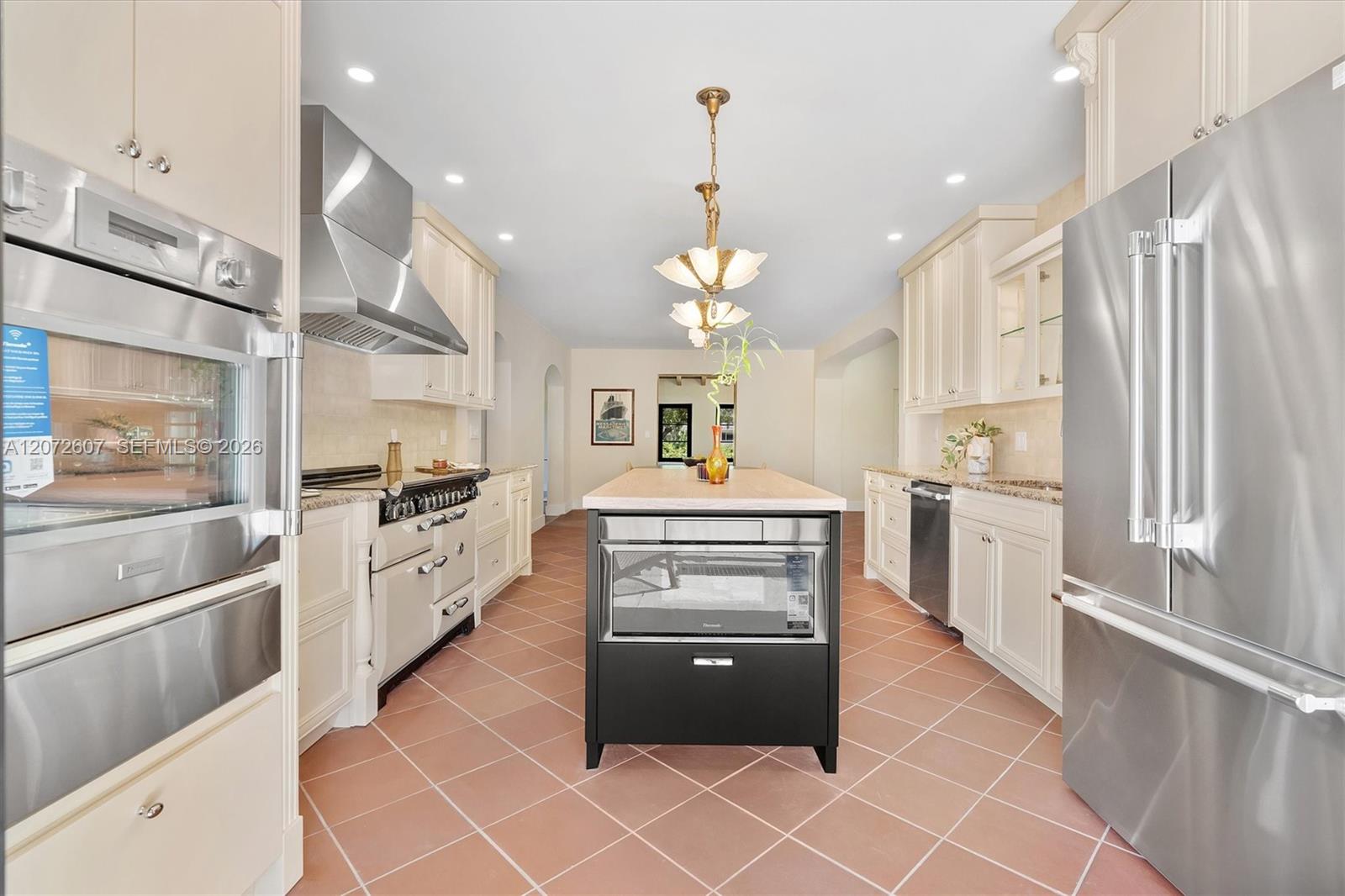 Kitchen with a large island, cream cabinetry, stainless steel appliances, and terracotta tile floors.