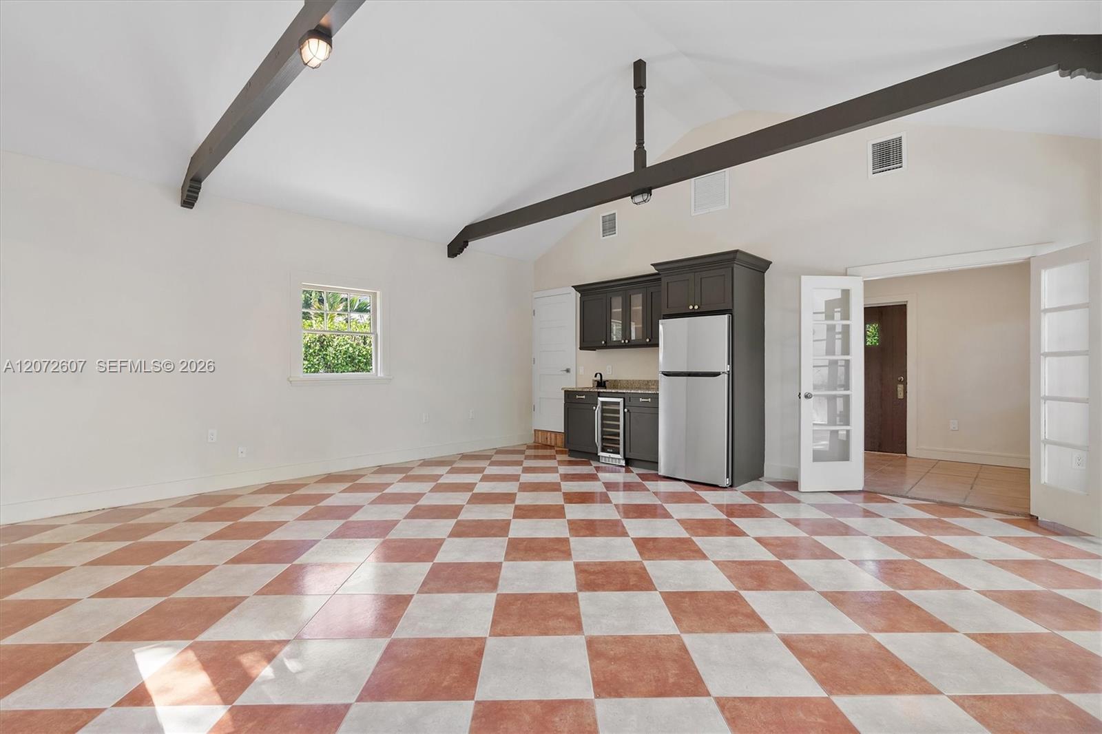 Open room with a compact kitchenette, checkerboard tile floor, and dark beams on a vaulted ceiling.