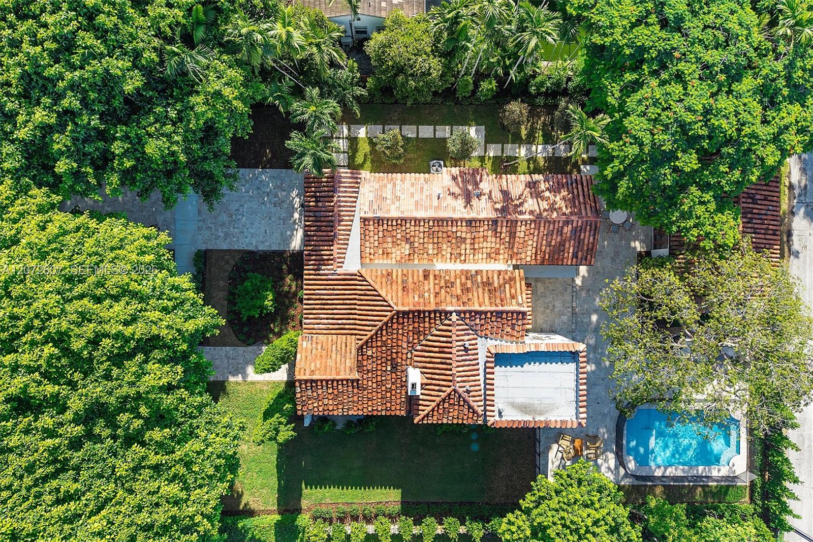Aerial view of a tile-roofed home and tropical backyard with a swimming pool.