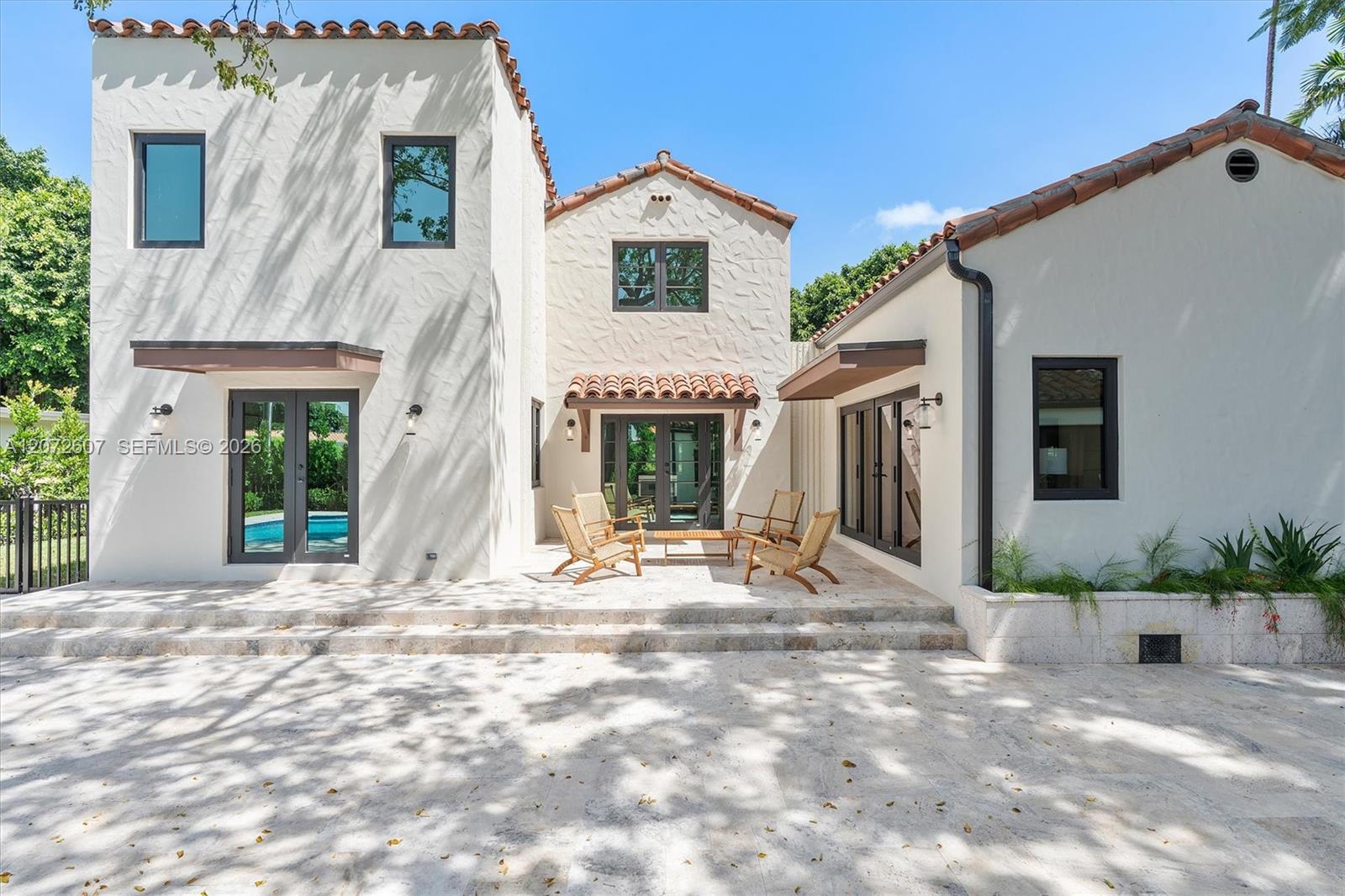 White stucco home with terracotta tile roofs surrounding a stone patio and outdoor seating.