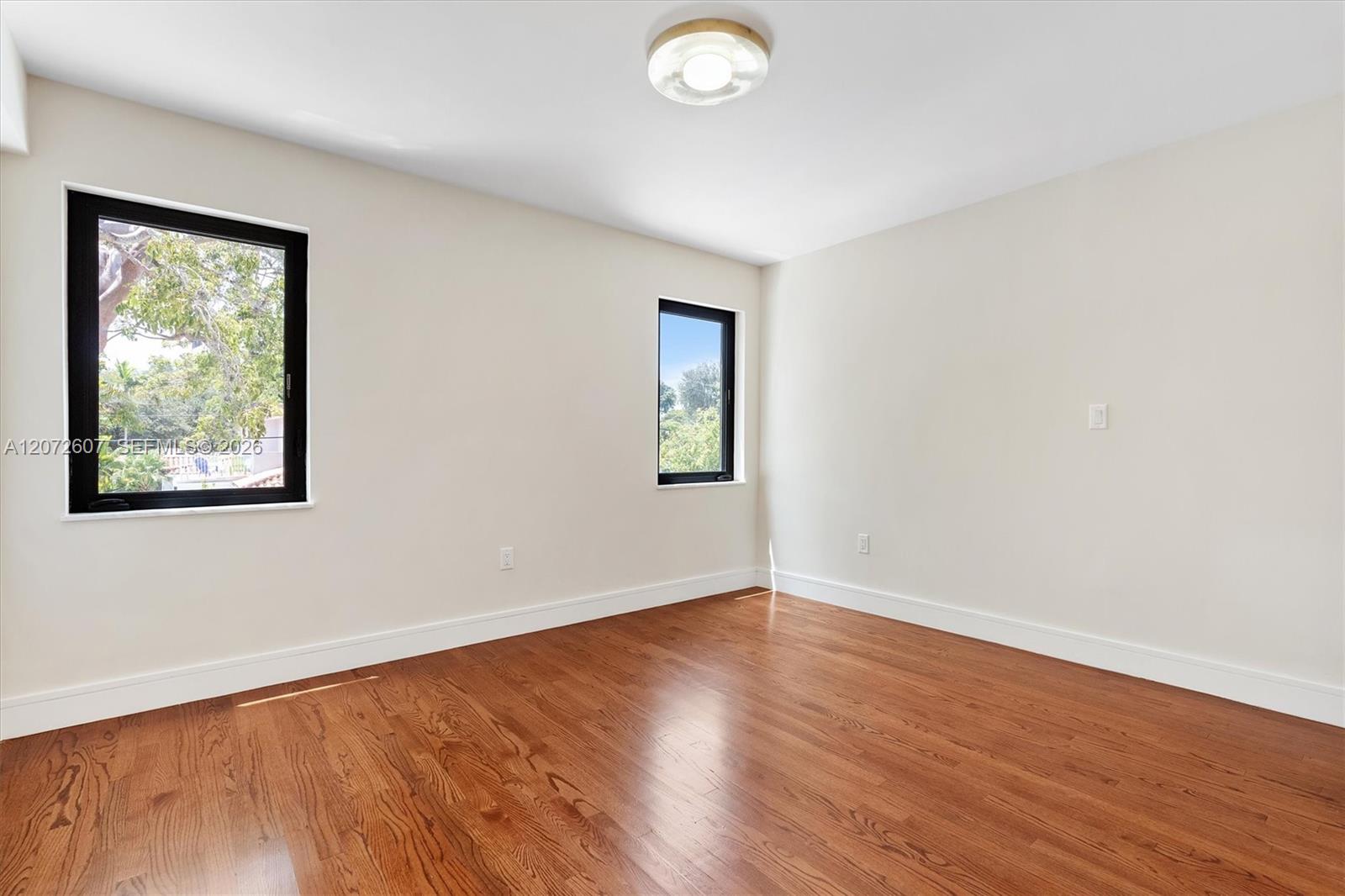 Empty room with polished hardwood floors and two black-framed windows.