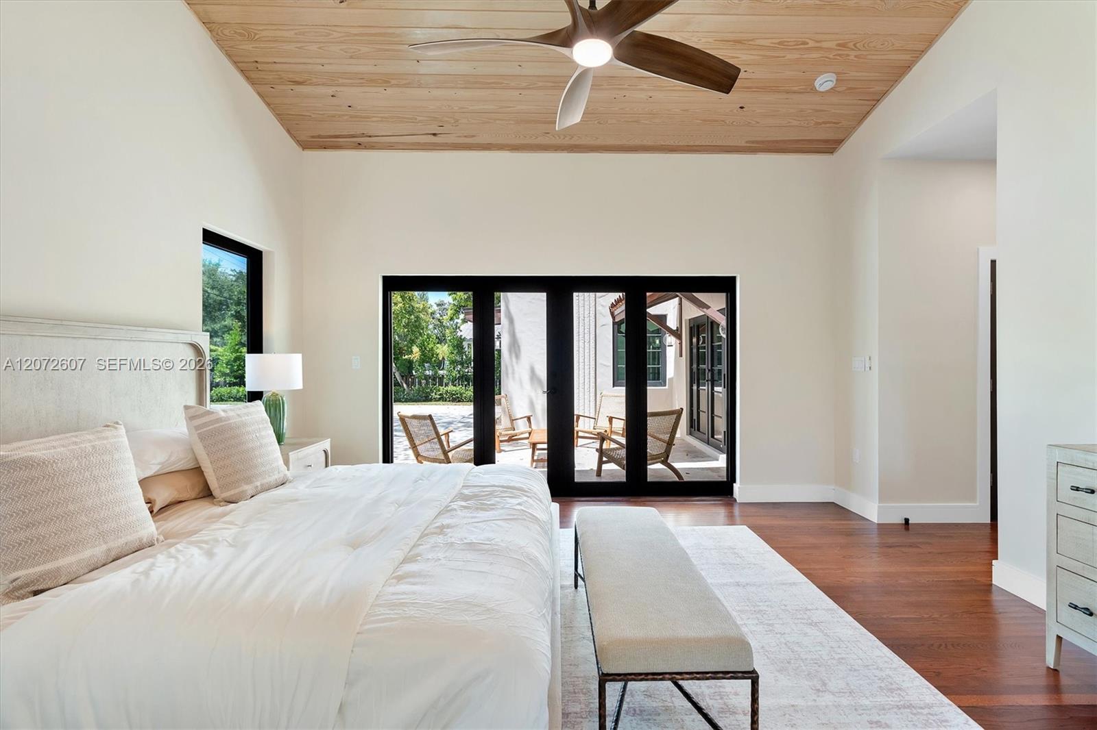 Staged bedroom with a wood plank ceiling, ceiling fan, and glass doors opening to a patio.