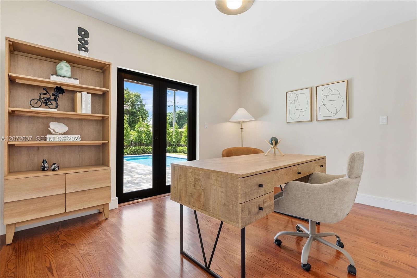 Furnished home office with built-in shelving and glass doors overlooking a backyard pool.