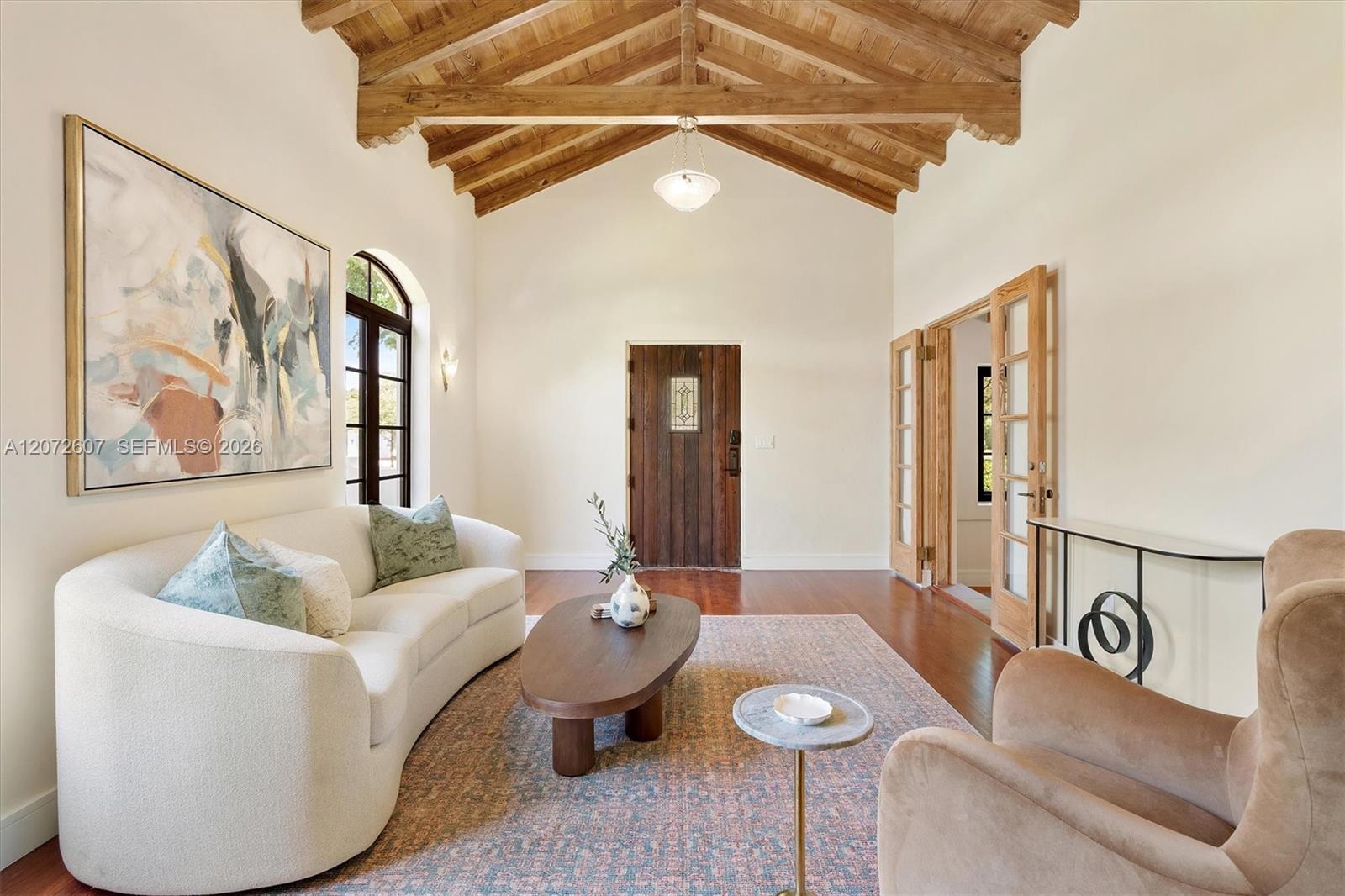 Living room with an exposed wood-beam ceiling, arched window, and curved white sofa.