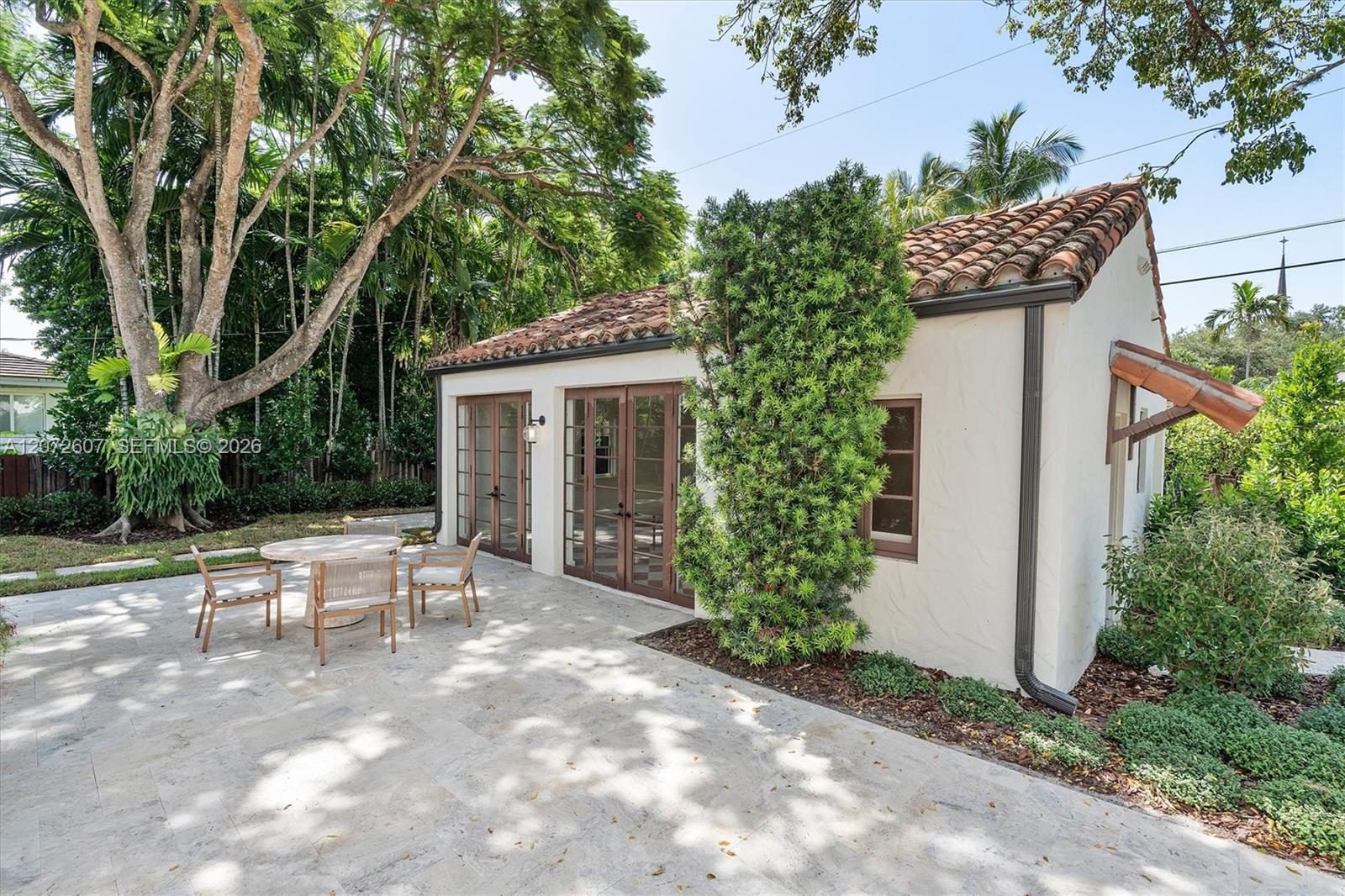 Home’s rear patio with stone paving, outdoor table and chairs, and lush tropical landscaping.
