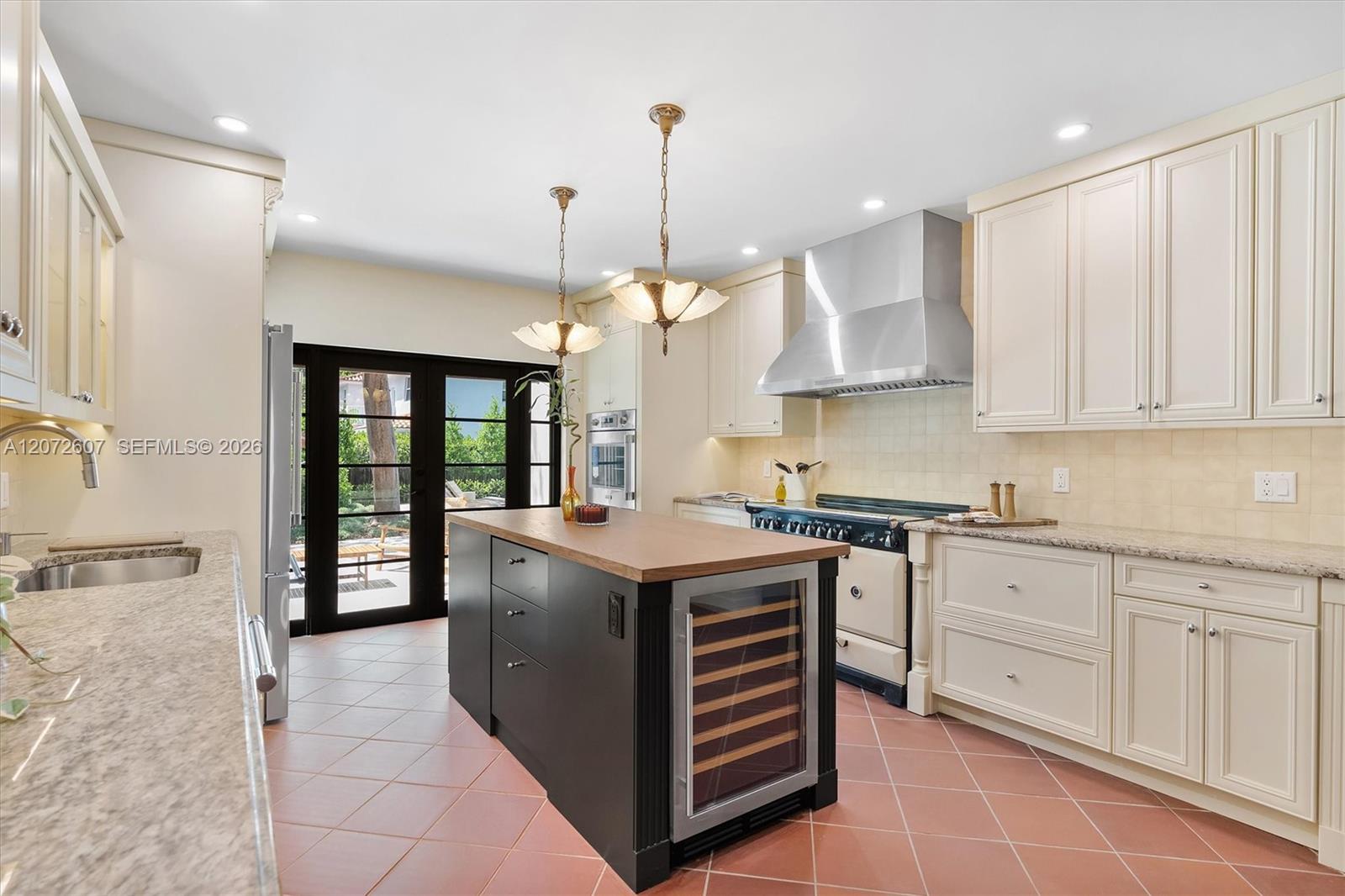 Kitchen with a dark wine-cooler island, cream cabinets, and glass doors opening to a garden.
