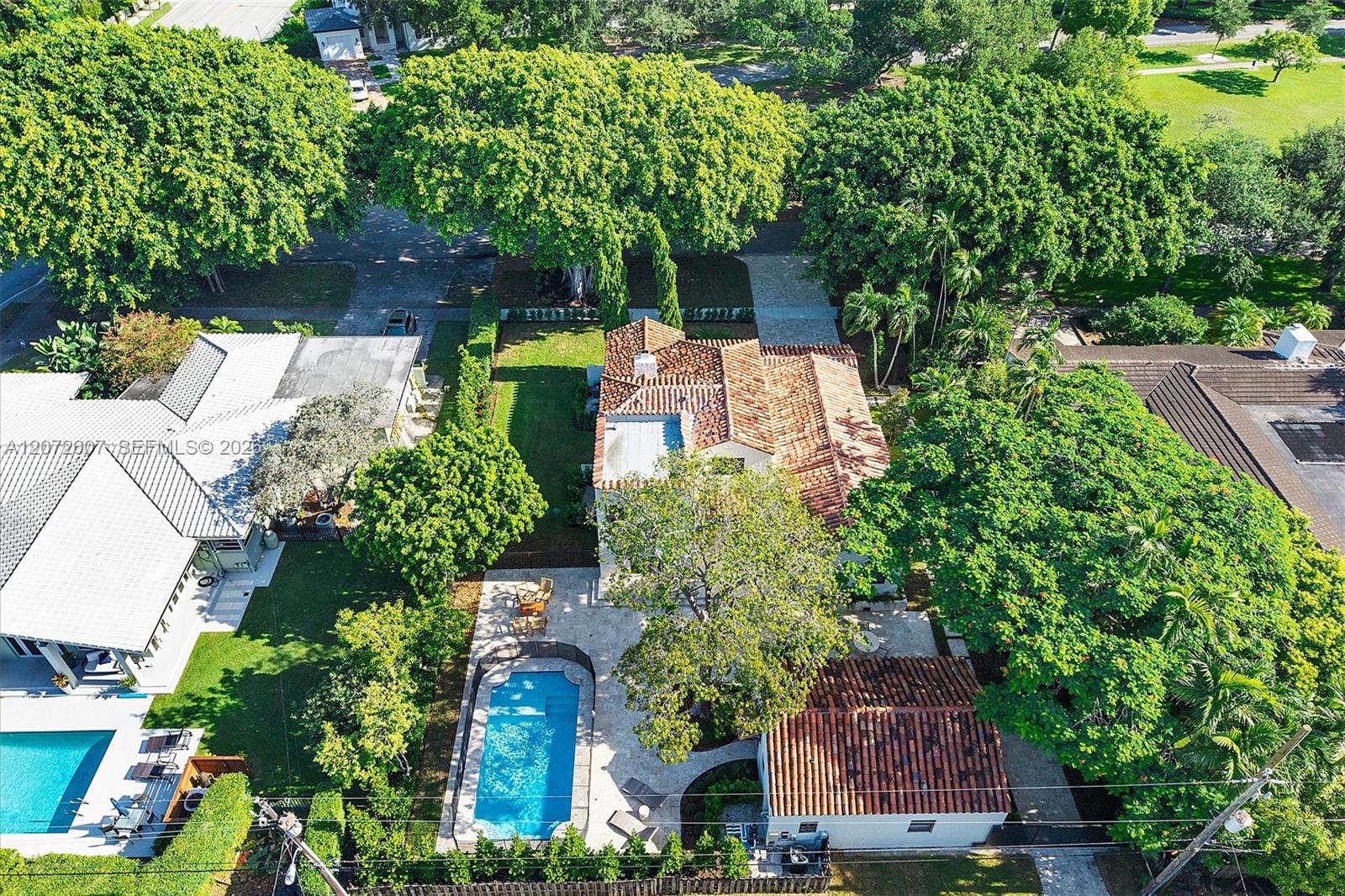 Aerial view of a terracotta-roofed home with a backyard pool, stone patio and mature trees.