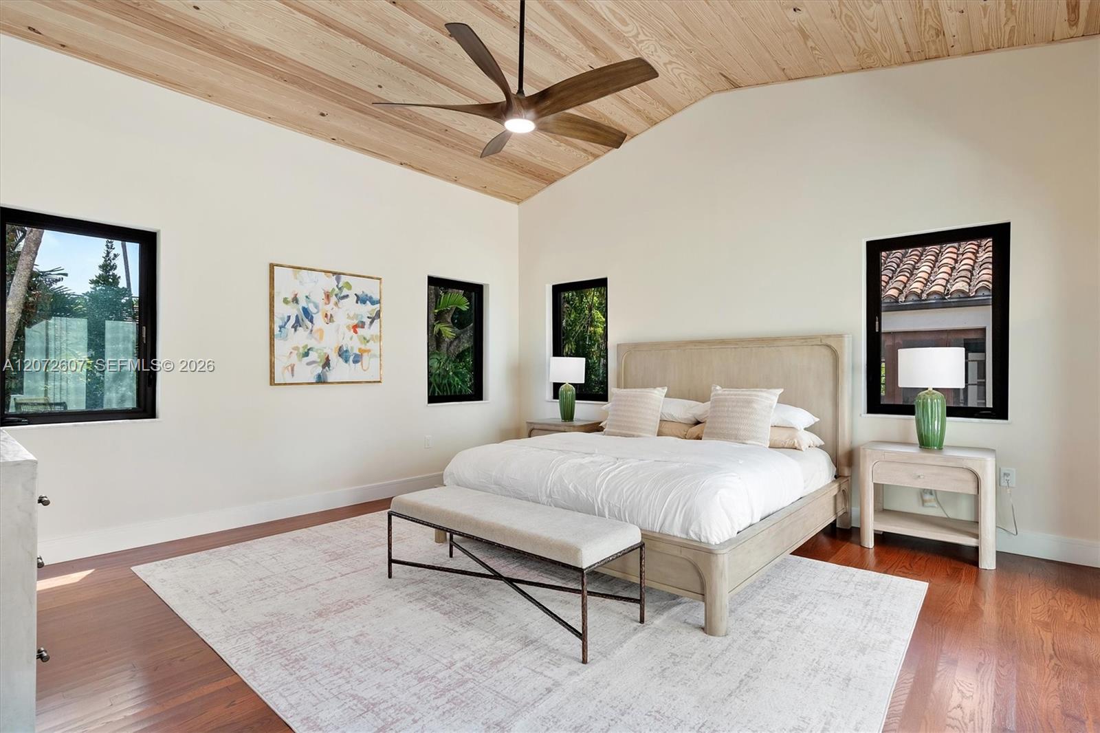 Furnished bedroom with a vaulted wood ceiling, ceiling fan, and large bed.
