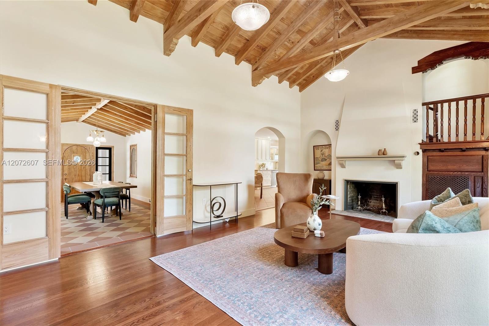 Living room with vaulted wood-beam ceiling, fireplace, hardwood floors, and an adjoining dining room.