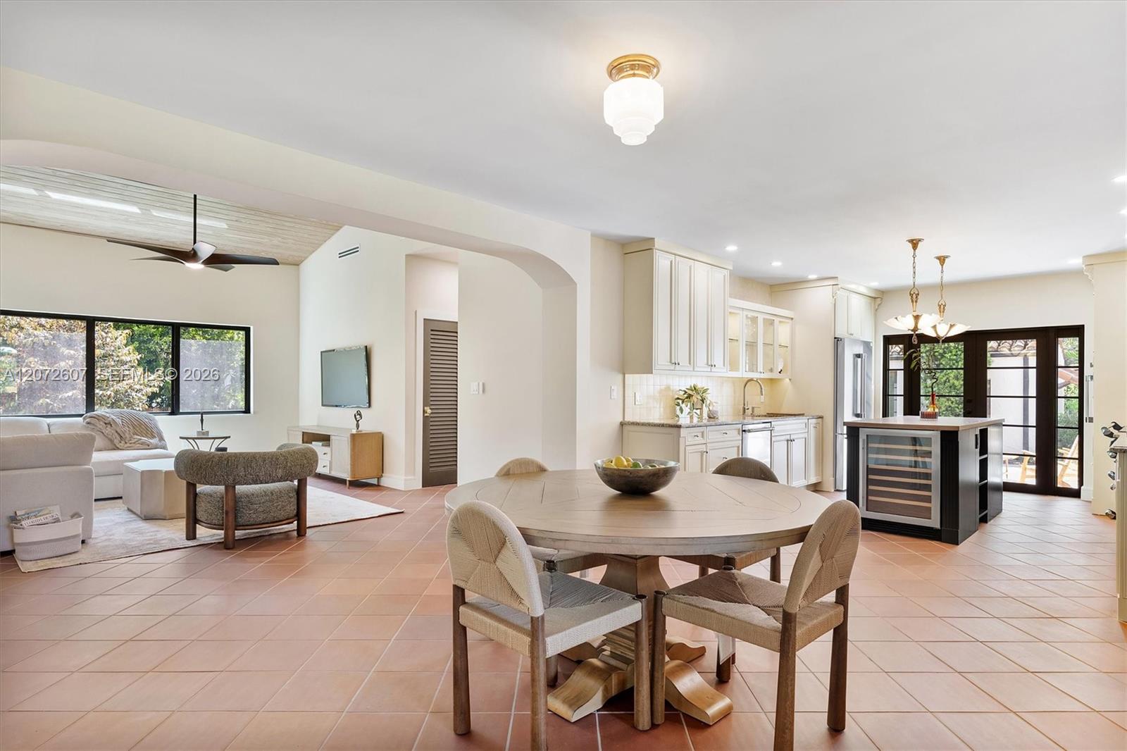 Open-plan dining area with a round table, white kitchen, and living room beside large windows.