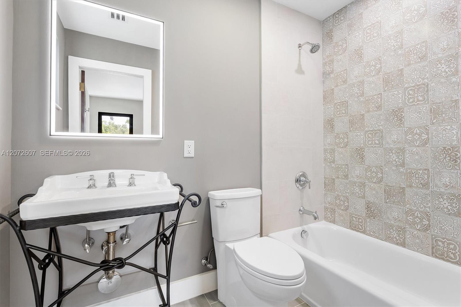 Bathroom with a console sink, toilet, and bathtub beside a patterned tile shower wall.