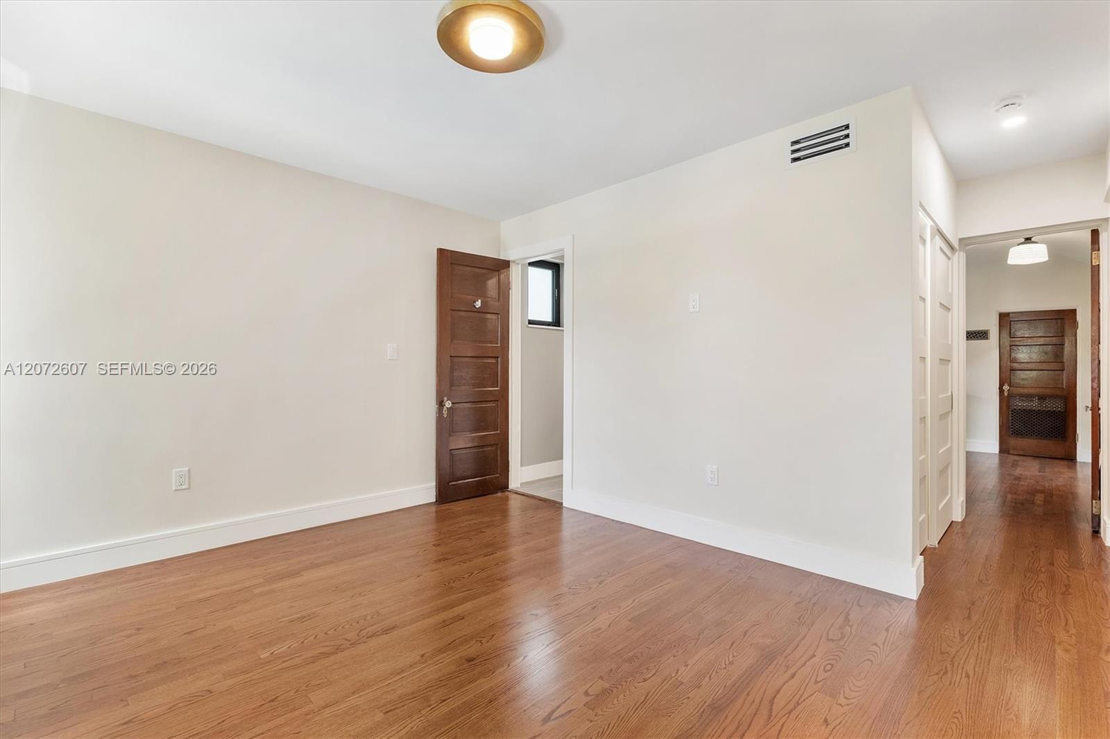 Empty room with warm hardwood floors, white walls, and a dark wood door.