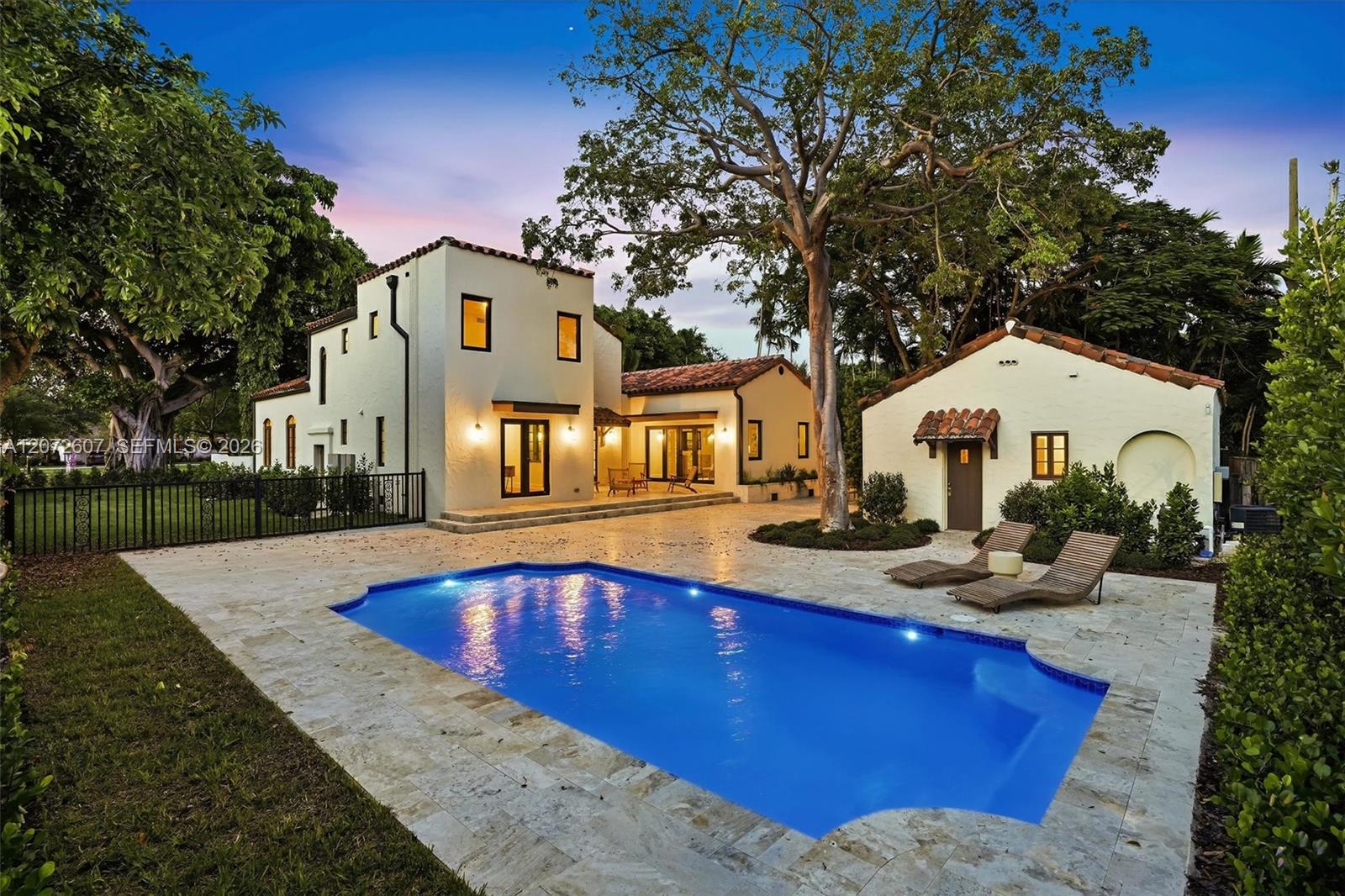 Spanish-style home with a blue swimming pool, stone patio, and lounge chairs at dusk.
