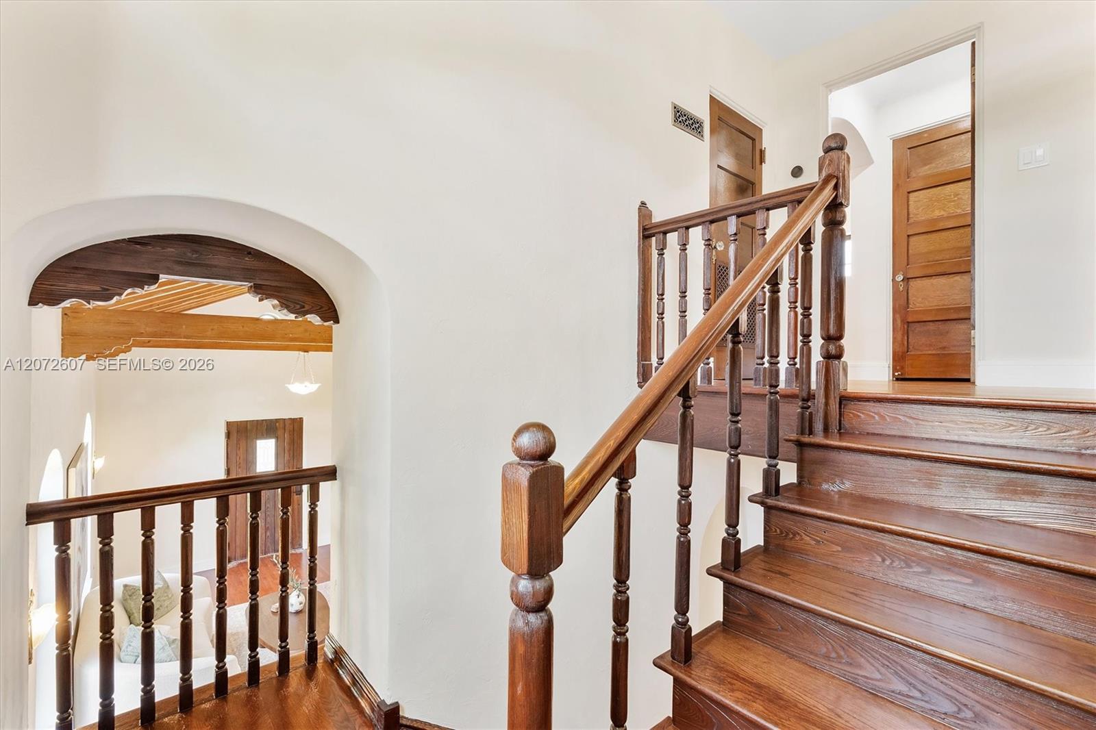 Wooden staircase and landing with turned railings beside an arched opening to the living area.