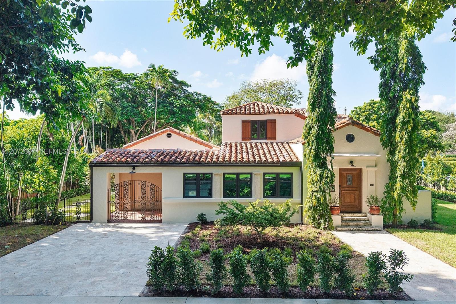 Cream stucco home with terracotta tile roof, gated driveway, and mature trees.