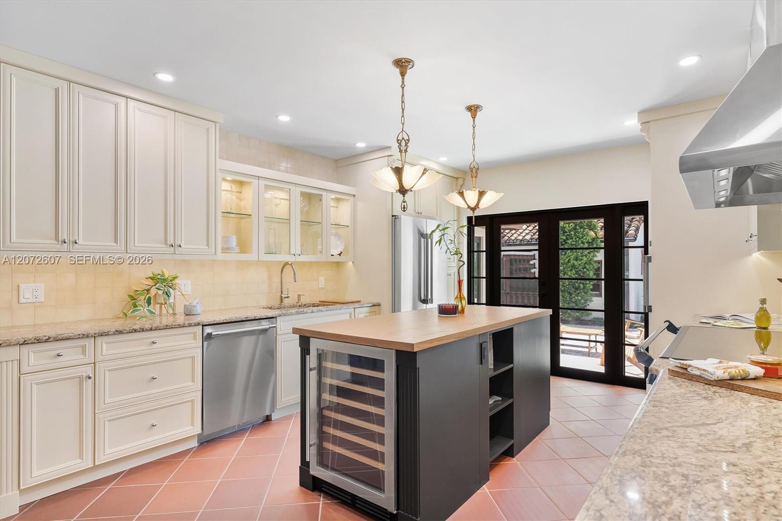 Kitchen with cream cabinetry, terracotta tile, and a dark island with built-in wine refrigerator.