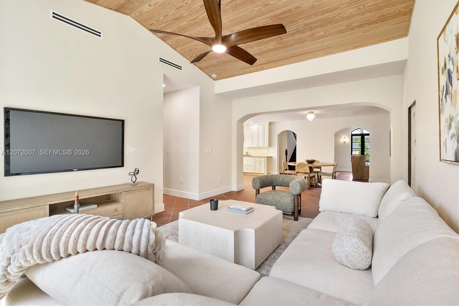 Living room with a white sectional, terracotta tile floor, and wood-plank ceiling with a fan.