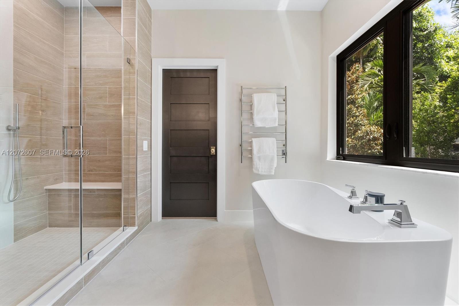 Modern bathroom with a freestanding tub, glass shower, and large window overlooking greenery.