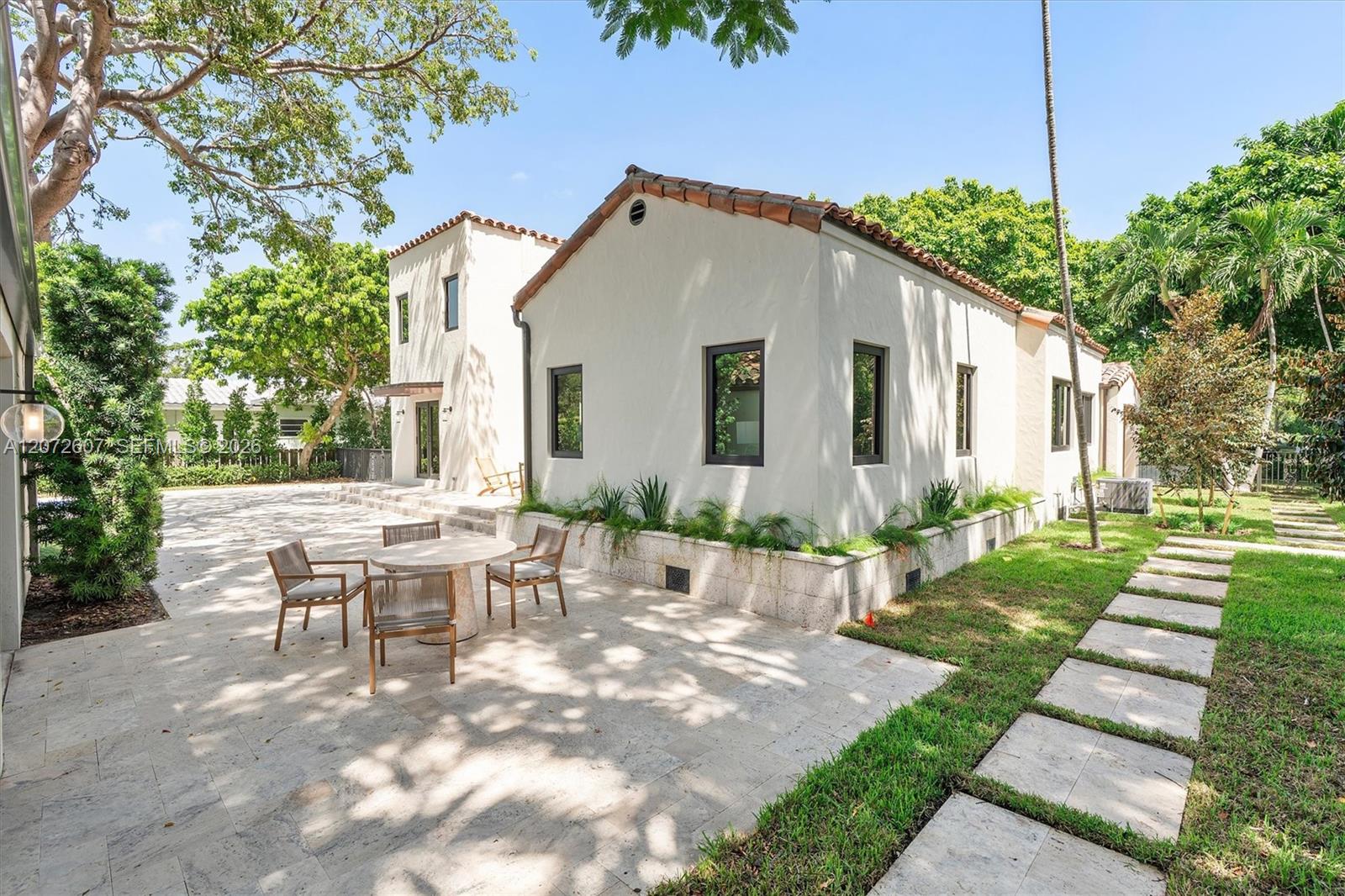 White stucco home with terracotta roof beside a paved patio and tropical landscaping.