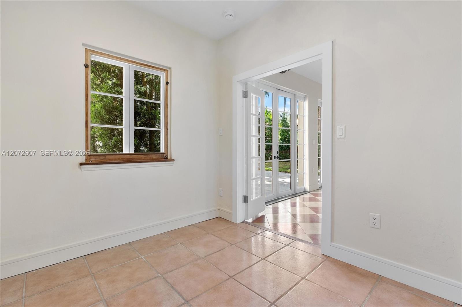 Empty tiled room with a wood-trimmed window and French doors opening outside.
