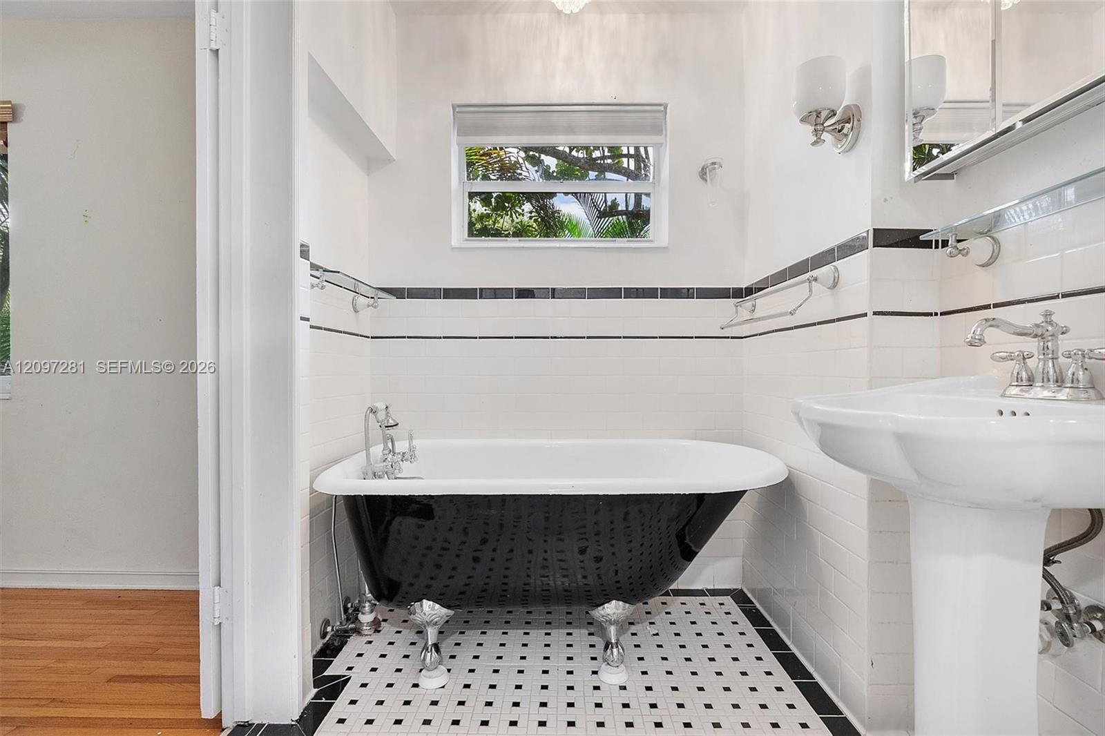Bathroom with a black clawfoot tub, pedestal sink, and black-and-white tiled floor.