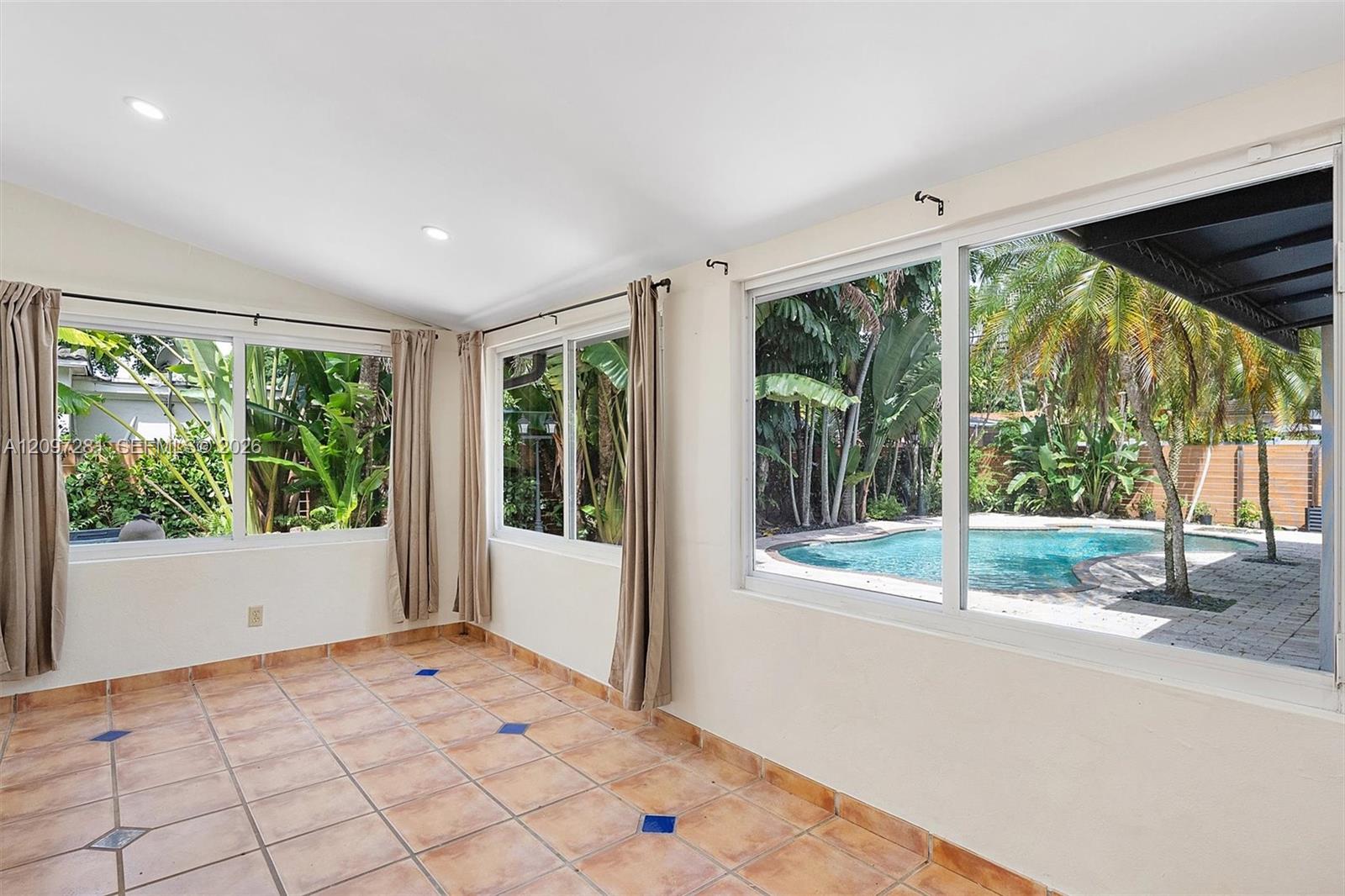 Tiled sunroom with large windows overlooking a tropical backyard pool.
