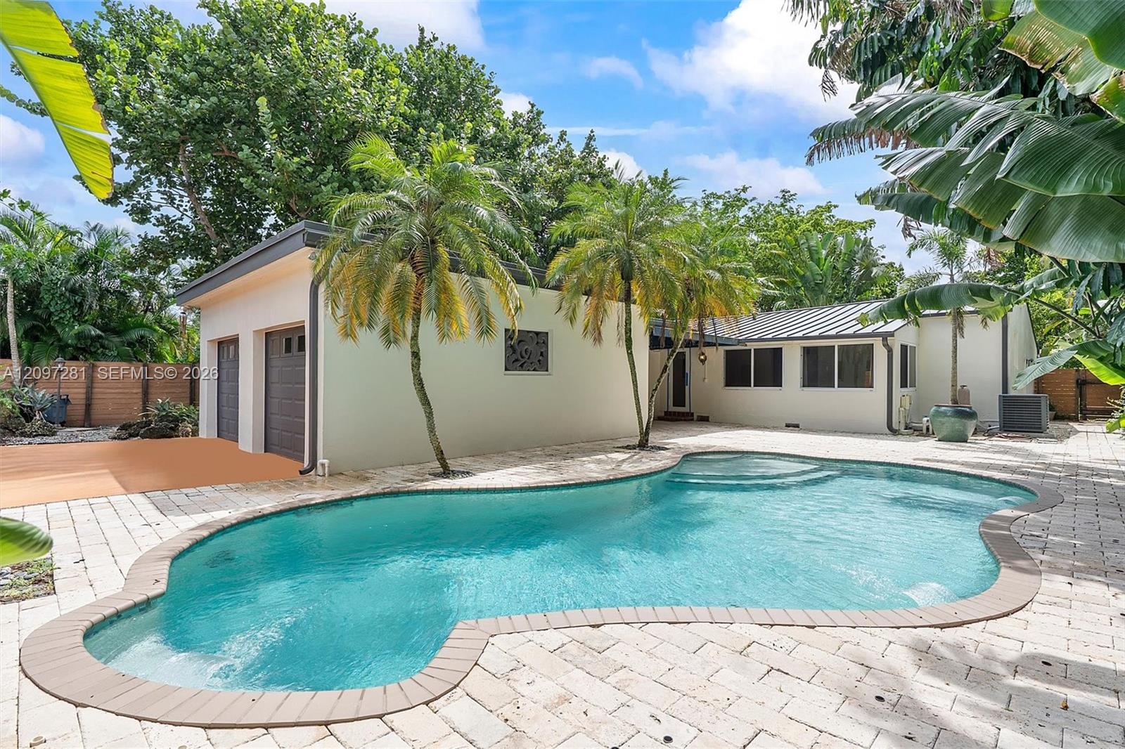 Backyard pool beside a single-story home, framed by palms and a pale stone patio.