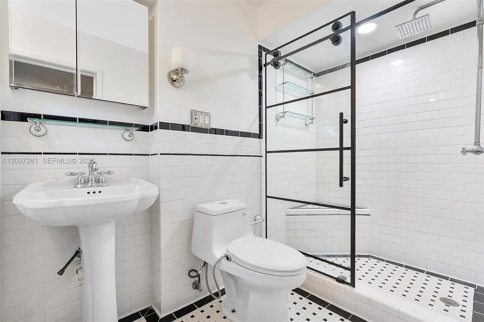 Bathroom with a black-framed glass shower, white subway tile, pedestal sink, and toilet.